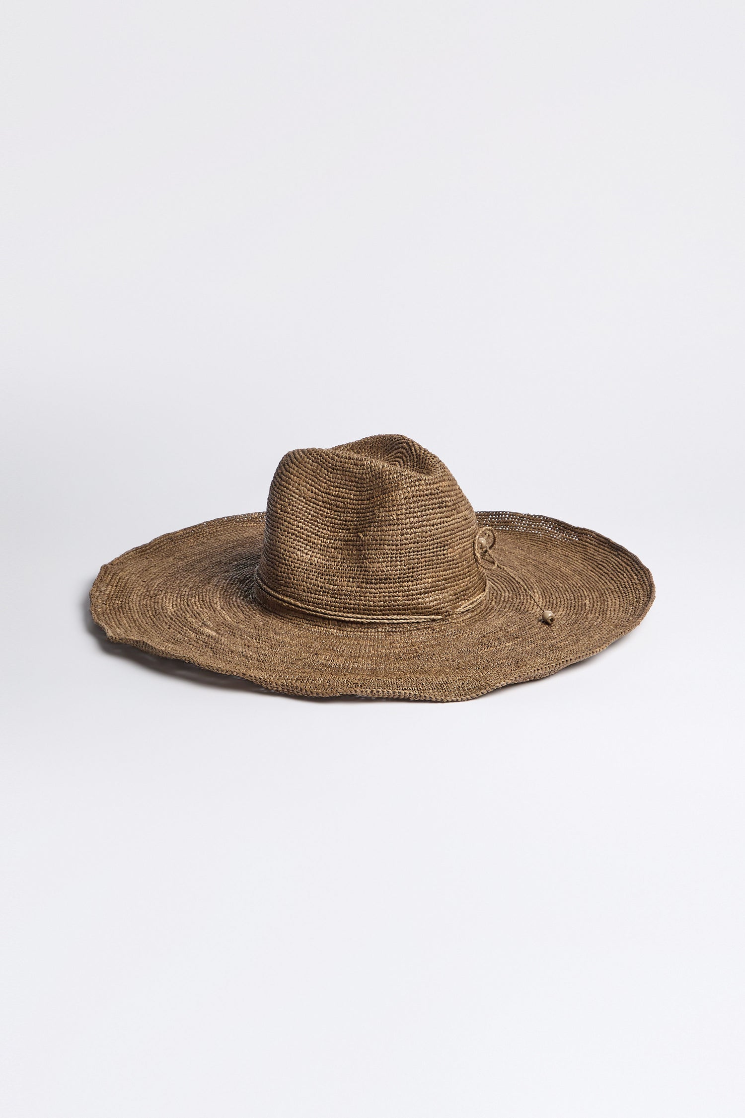 A Hand Woven Double Crochet Raffia Hat, featuring a wide brim and elegant adjustable fit, is crafted from Madagascan raffia and displayed on a plain white surface.