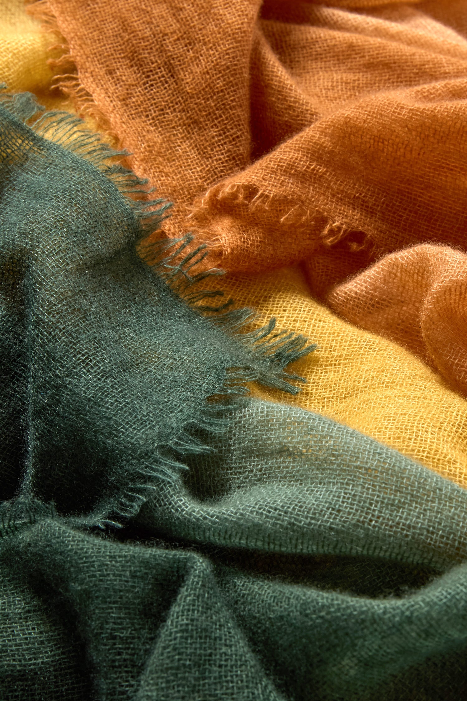 Close-up of the Soft Colourblend Cashmere Shawl, showcasing its textured, loosely woven fabric in a green-to-yellow-to-orange ombré gradient with frayed overlapping edges.