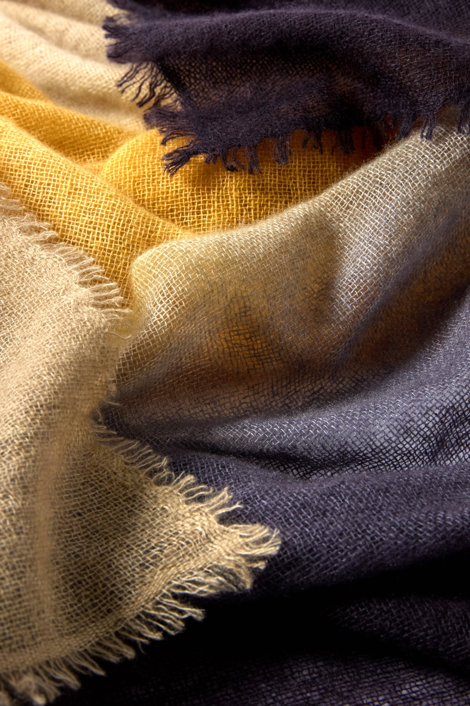 Close-up of the Soft Colourblend Cashmere Shawl, showcasing its layered, loosely woven design in beige, yellow, and dark gray with frayed edges—a timeless accessory for any wardrobe.