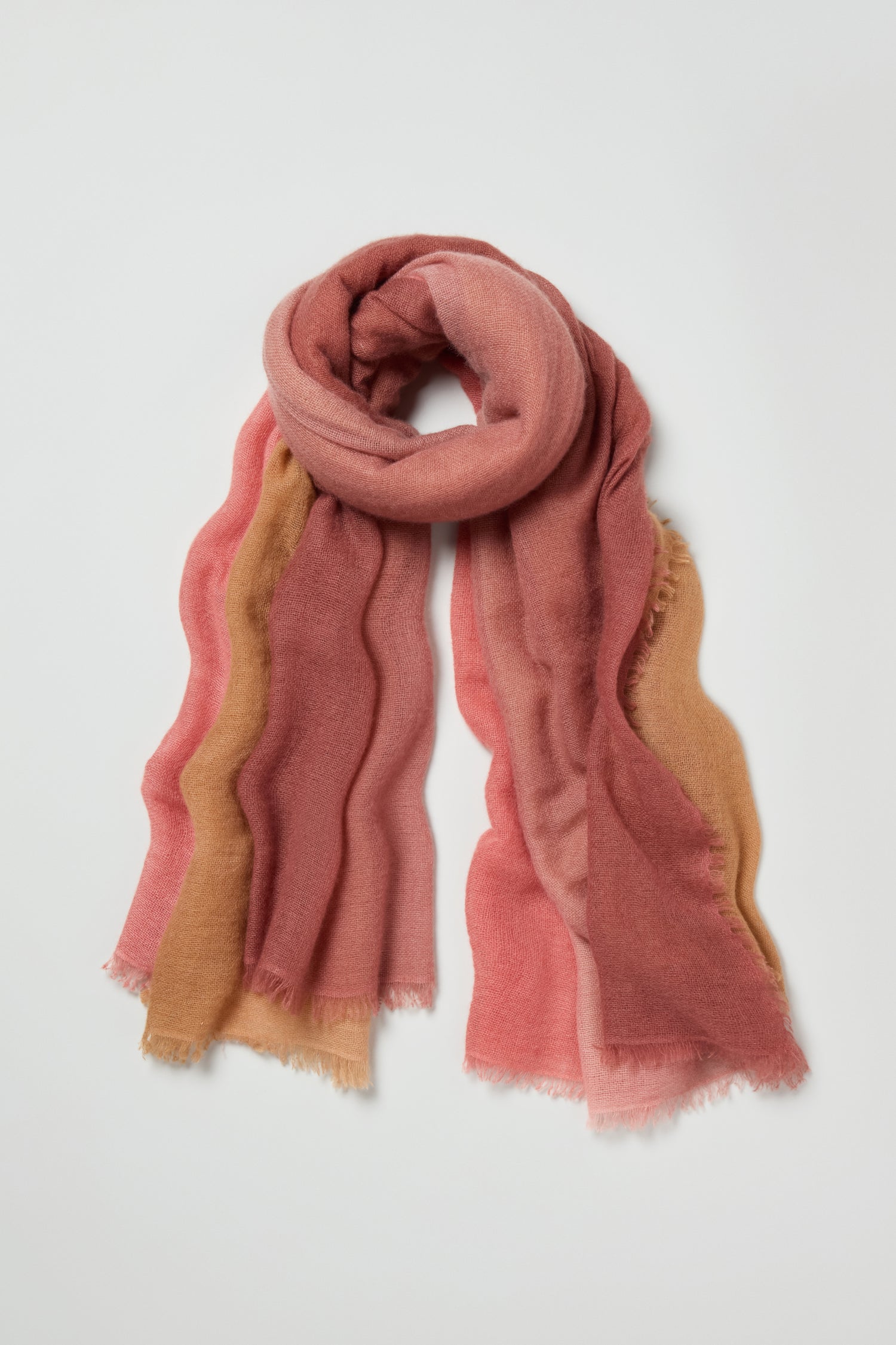 The Soft Colourblend Cashmere Shawl features wavy stripes in pink, coral, and tan, creating an elegant ombré gradient. This soft, lightweight scarf is shown laid flat on a white background.