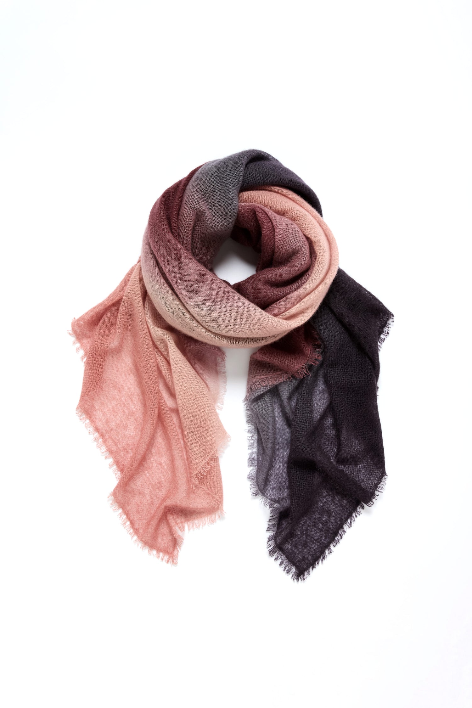 The Soft Colourblend Cashmere Shawl features a gradient from pink to dark gray, arranged in a loose spiral on a white background—a timeless accessory for any wardrobe.