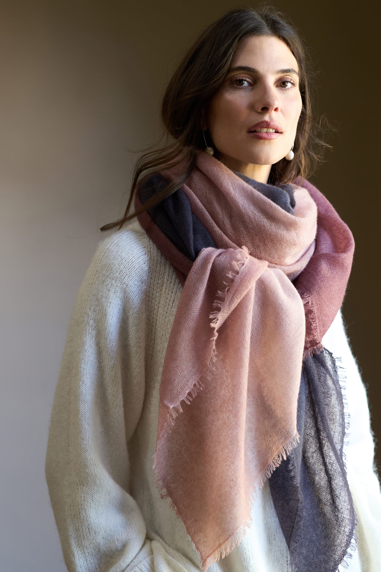 A woman wears a Soft Colourblend Cashmere Shawl over a cream sweater, standing against a neutral background.