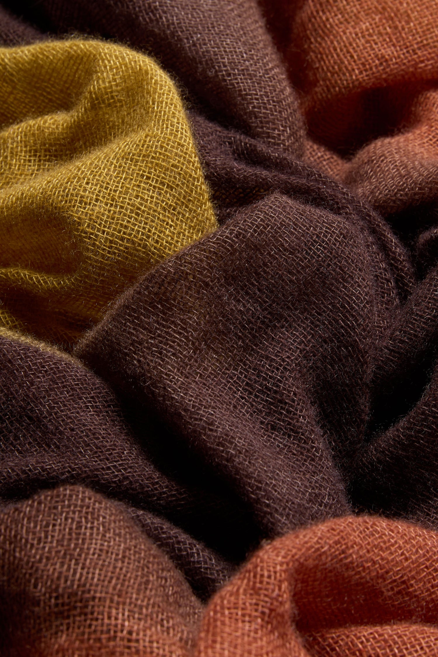 Close-up of textured, loosely woven fabric in shades of brown, orange, and yellow, arranged in soft, overlapping folds—a Rust and Ochre Soft Colourblend Cashmere Shawl made in Nepal.