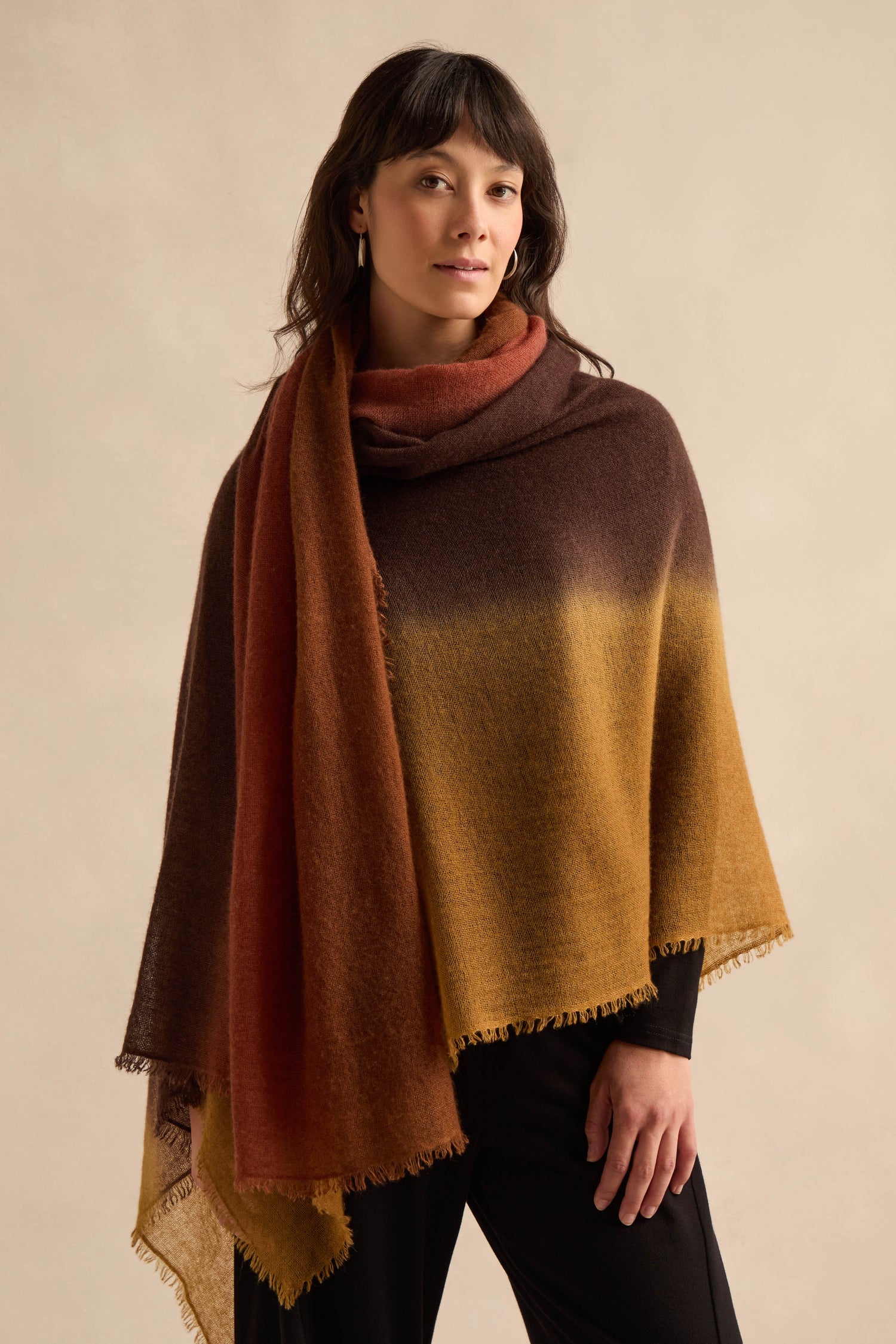 A person stands against a neutral background wearing the Rust and Ochre Soft Colourblend Cashmere Shawl over a black outfit.