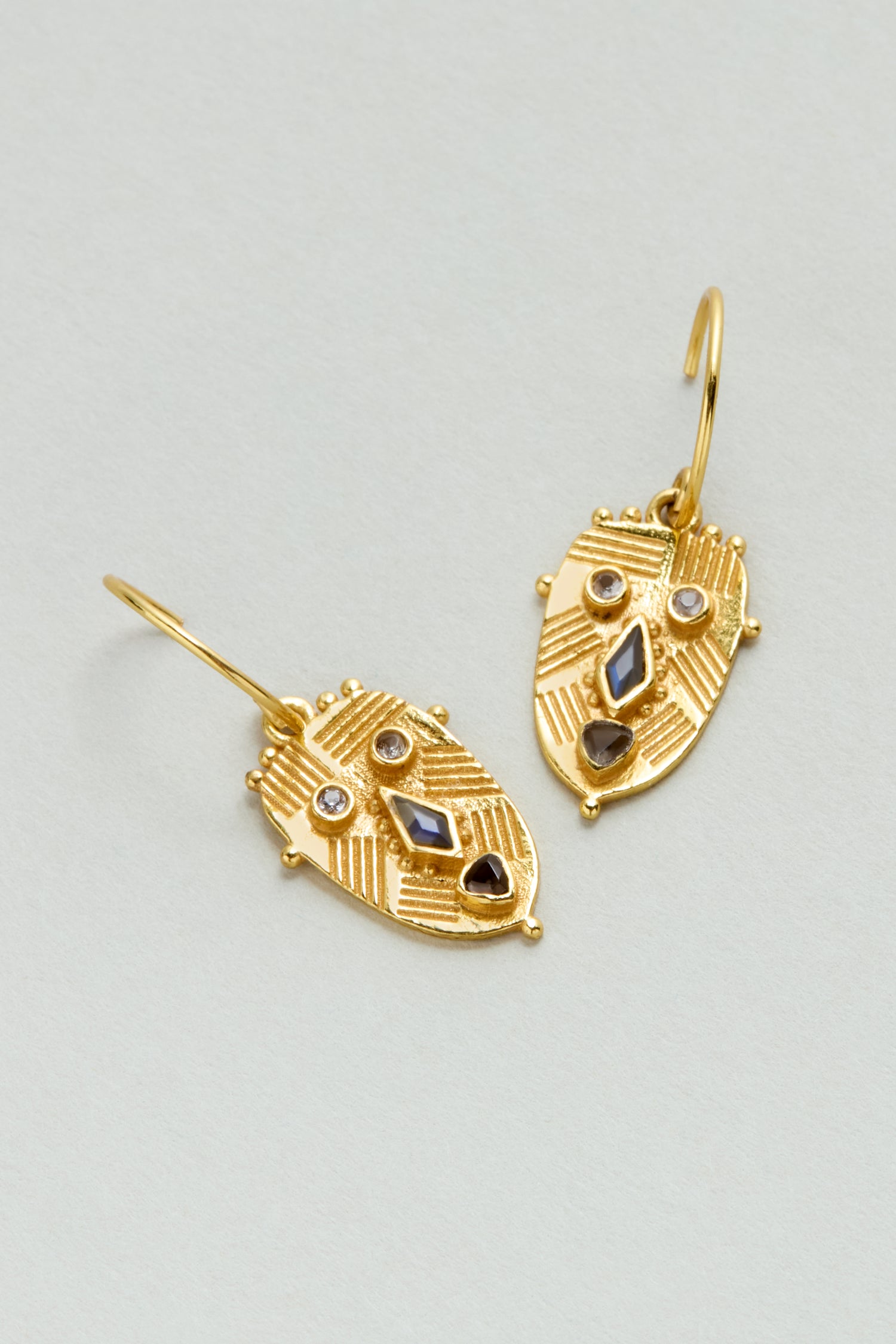The Gold Plated Labradorite Mini Faces Earrings feature geometric patterns with small dark and clear gemstone accents on a light gray background.