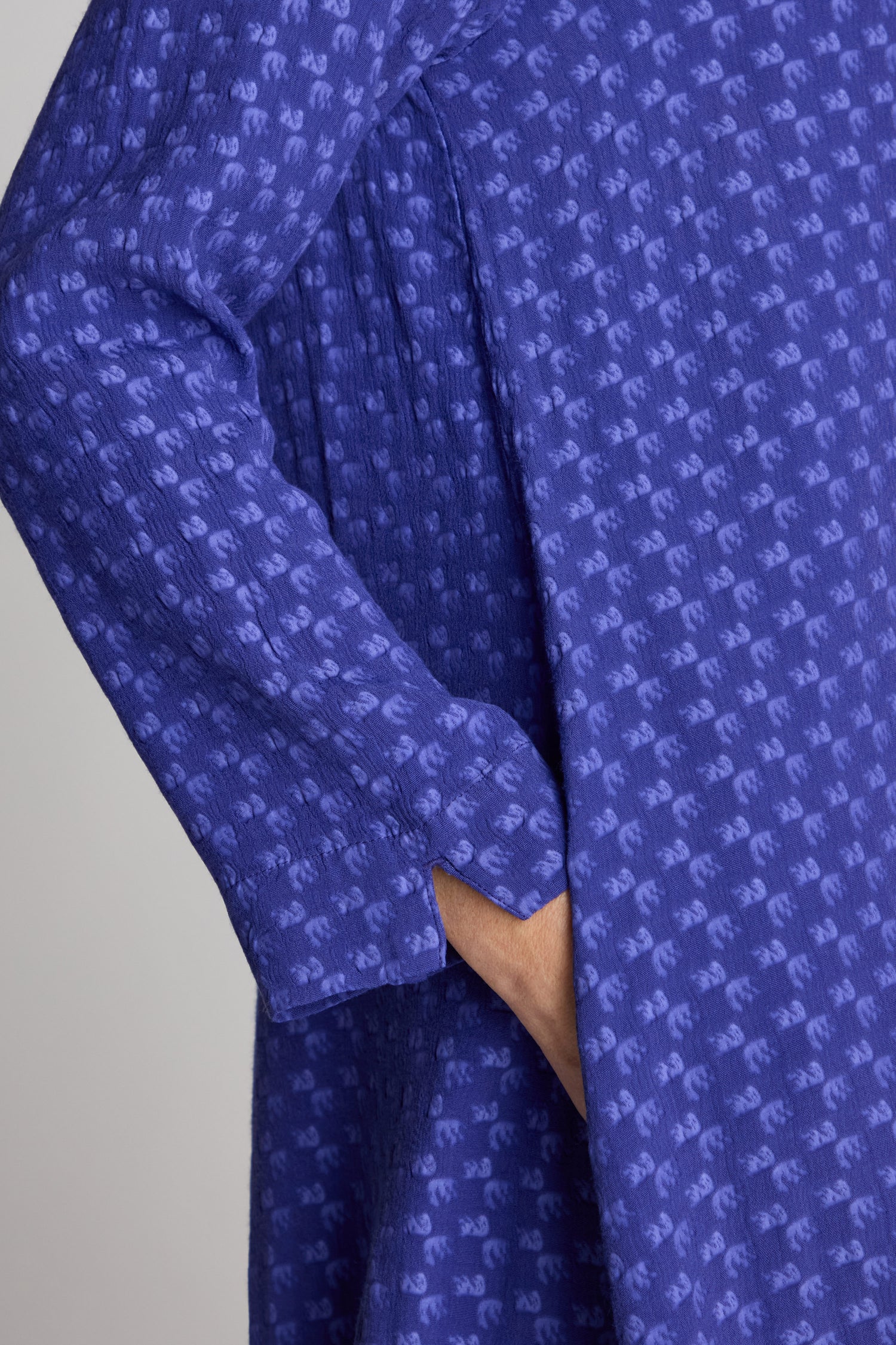 Close-up of a person’s arm and hand pocketed in a blue textured long-sleeve garment, identified as the Small Square Jacquard Bubble Dress.