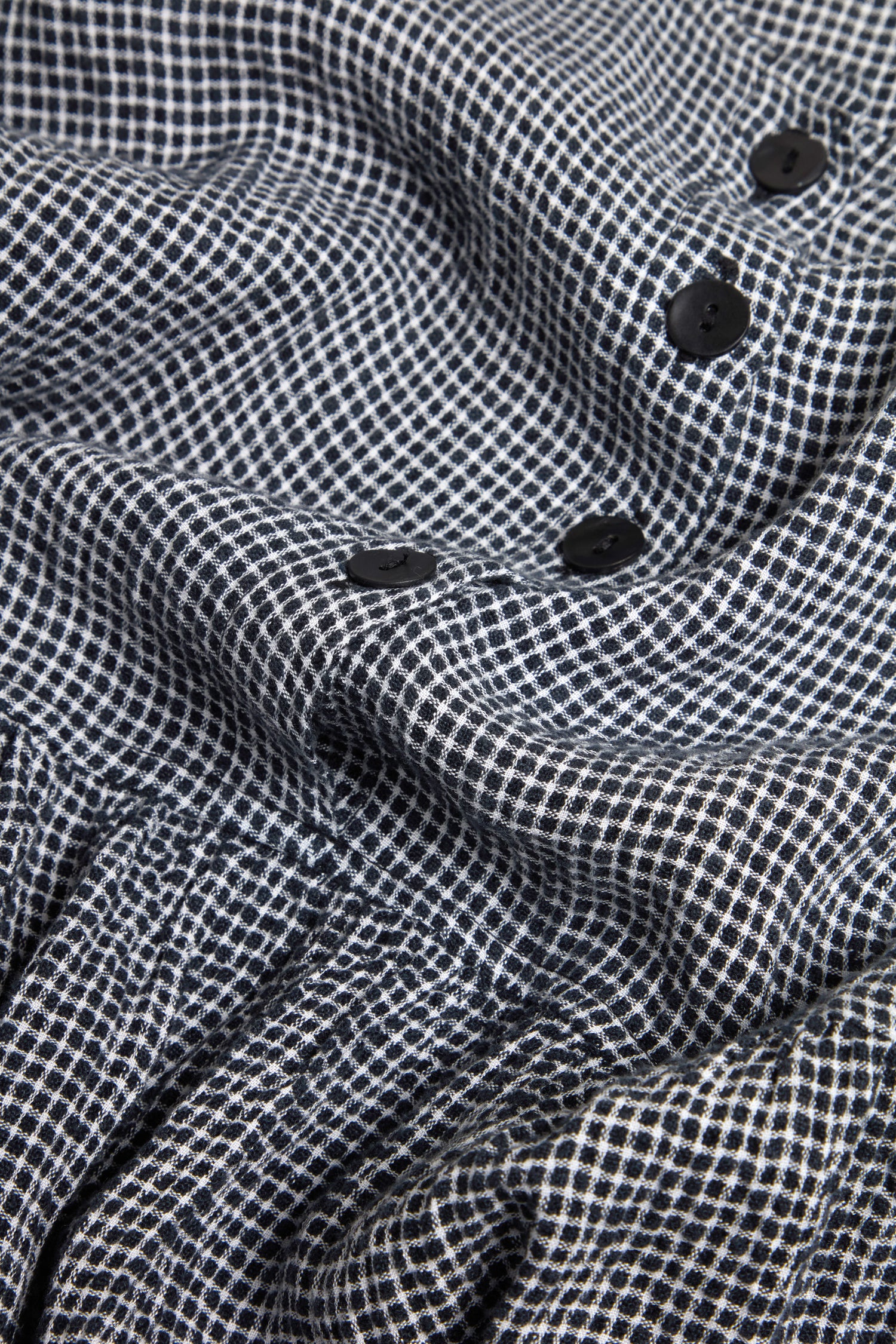 Close-up of the Micro Gingham Bubble Dress in black and white checks, model MTD6166-MGI, showcasing three black buttons on its textured surface.