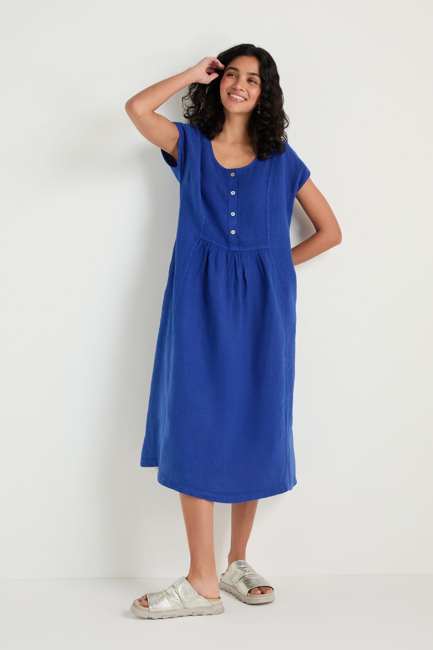 A woman stands against a plain white background, wearing the Linen Button Cerulean Placket Dress styled with silver sandals.