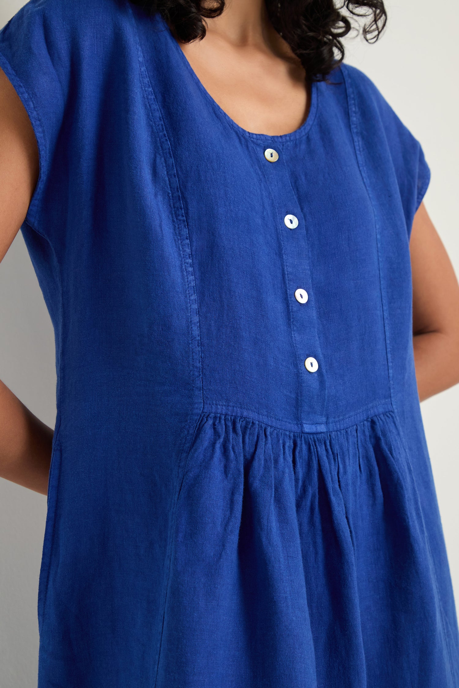 A person wears the Linen Button Cerulean Placket Dress, featuring a loose fit, short sleeves, and a button placket down the front.