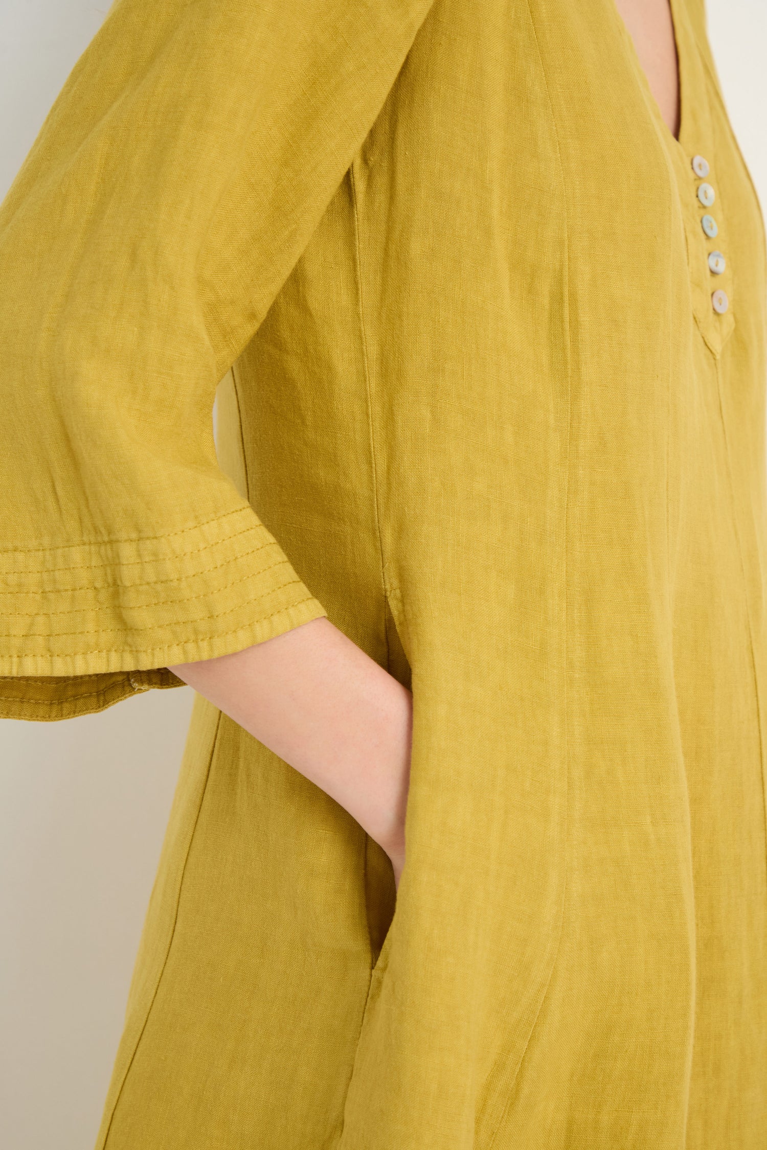 A person wearing the Linen Seam Golden Flare Dress, featuring three-quarter sleeves, panel seams, a buttoned neckline, and side pockets, casually places one hand in a pocket.