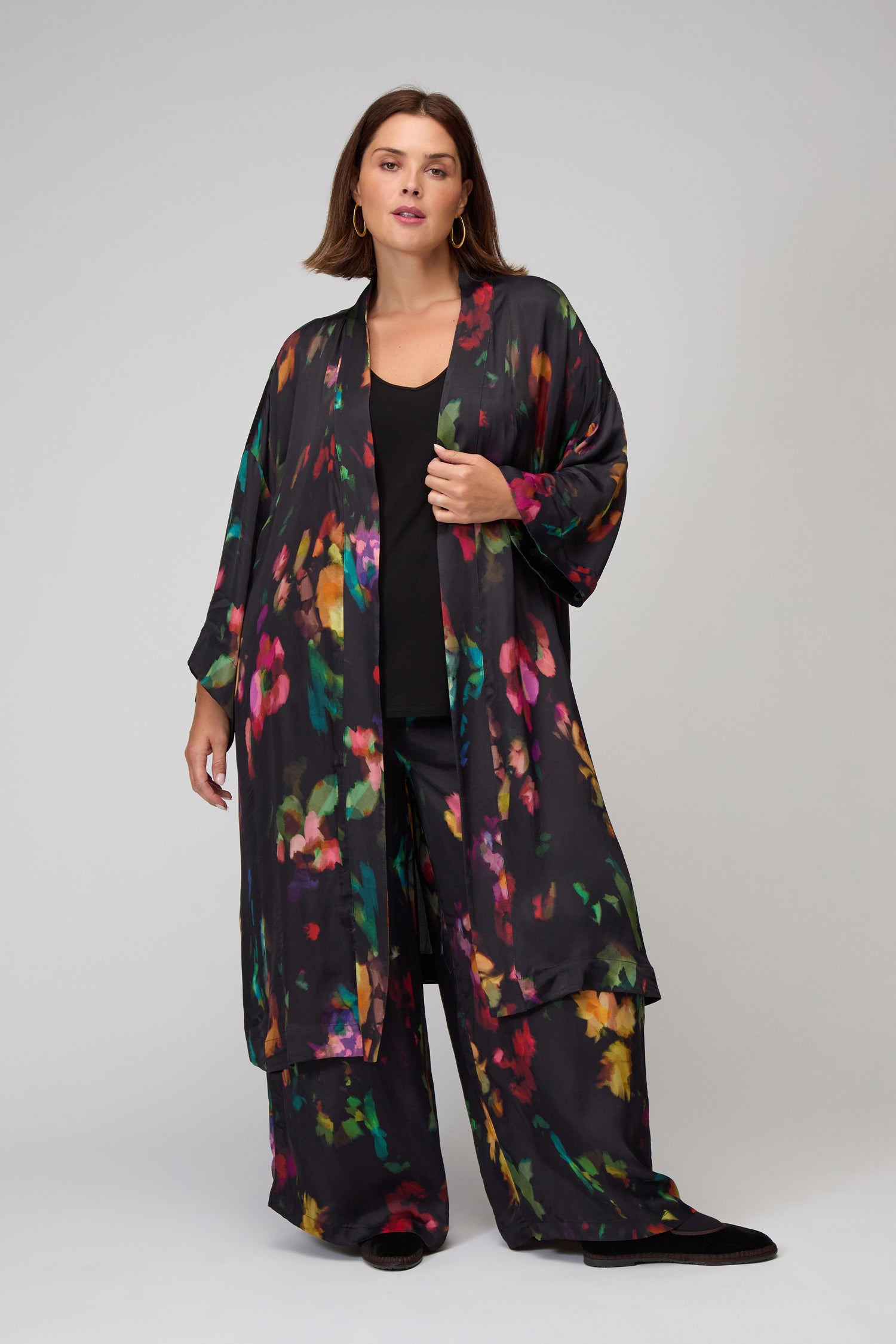 A woman models the Winter Floral Kimono, featuring a vibrant floral print and paired with wide-leg pants, standing against a plain background.