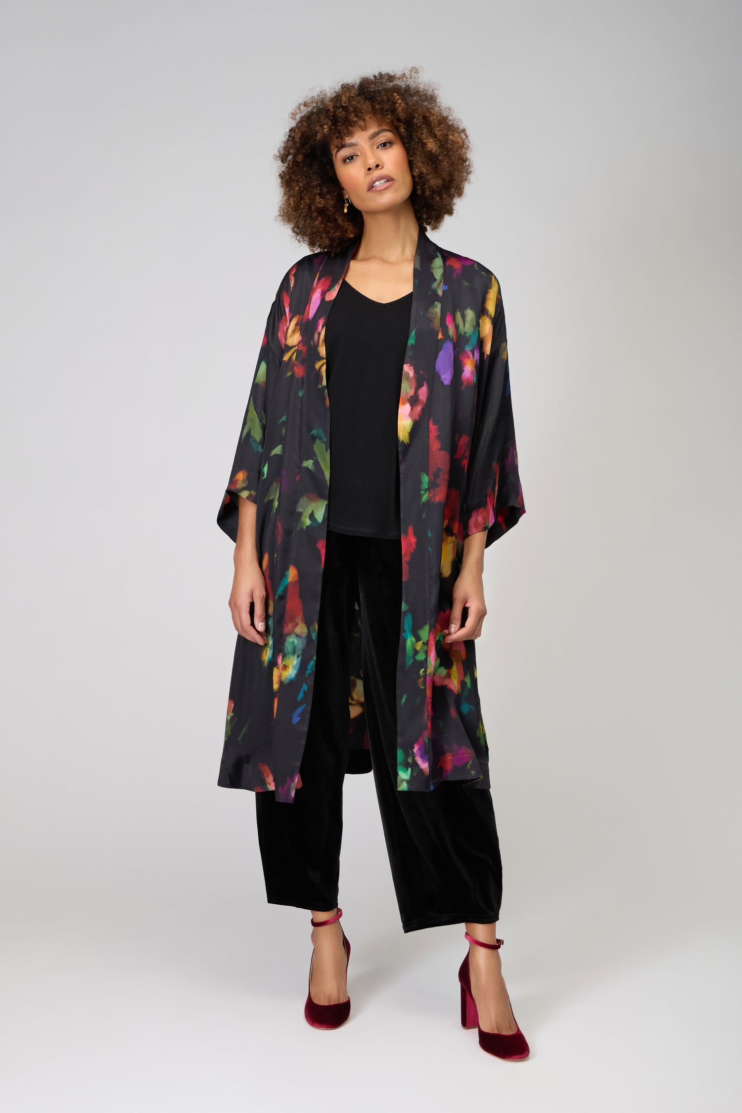 A person stands against a plain background wearing the Winter Floral Kimono, featuring a painterly floral print in black, paired with a black top, black pants, and red velvet heels.