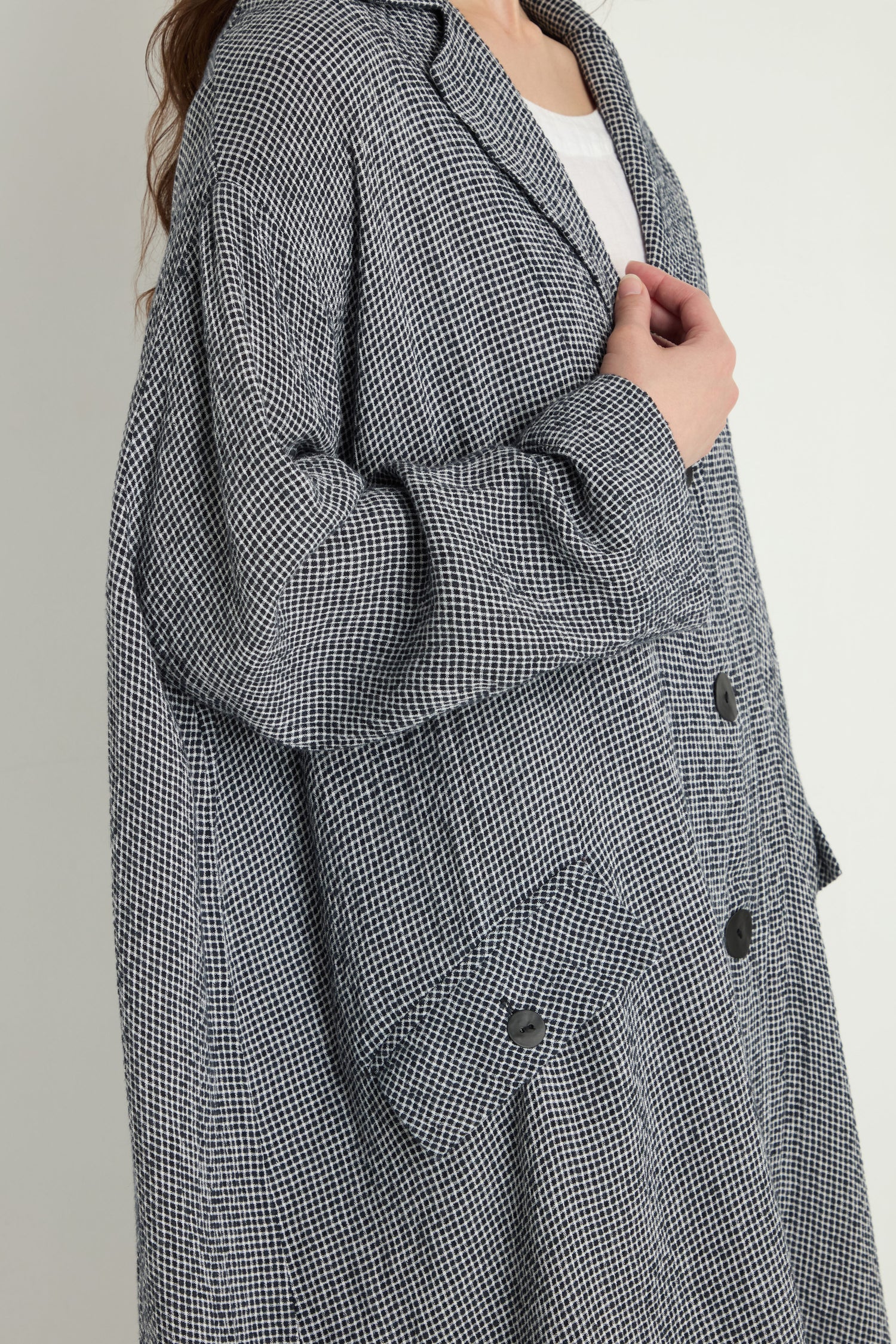 A person wearing the Micro Gingham Boxy Coat over a white top, holding it closed with one hand—much like securing a valuable electronic component.
