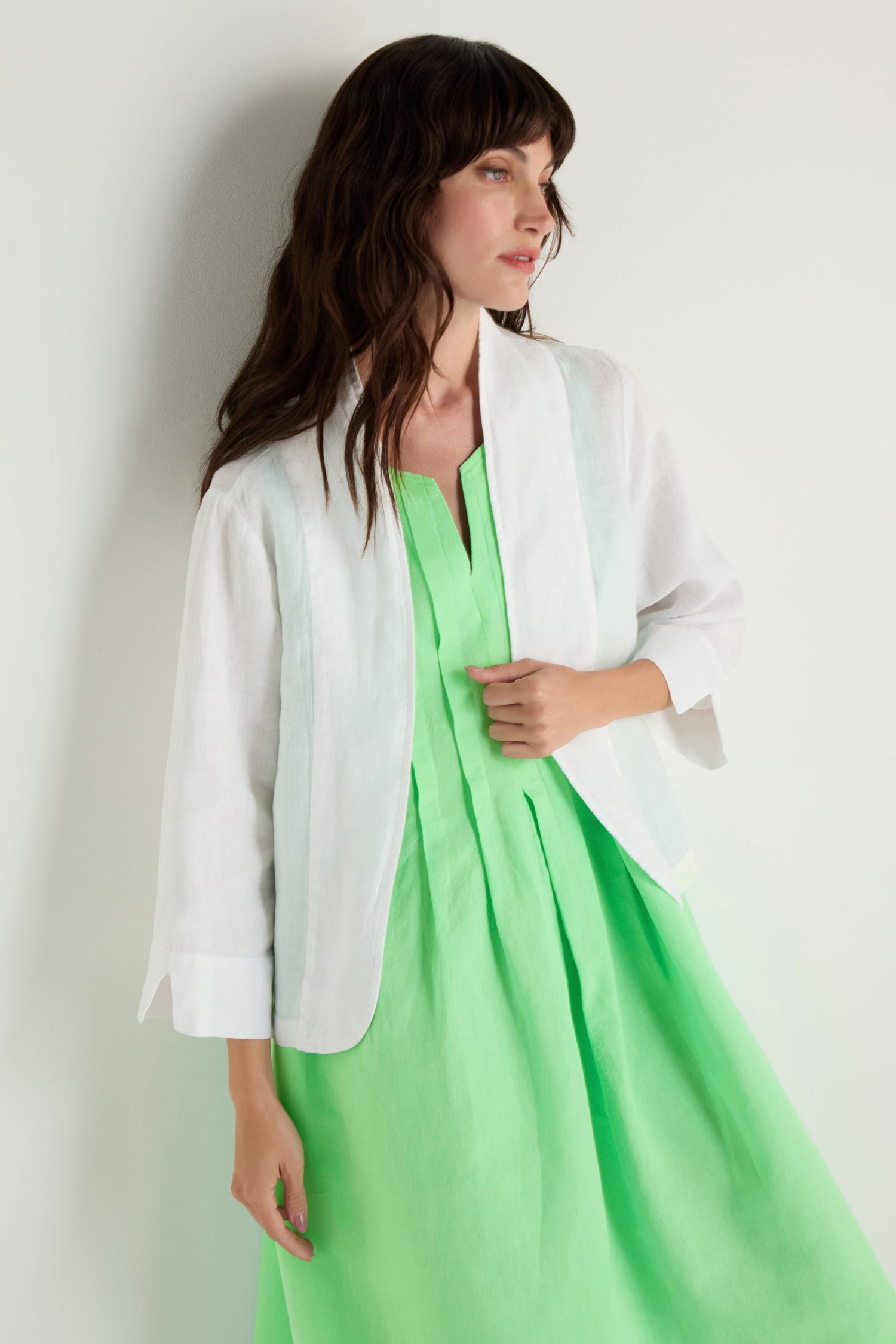 A woman stands against a plain white background, wearing a light green dress paired with the White Linen Cropped Jacket featuring an edge-to-edge front.