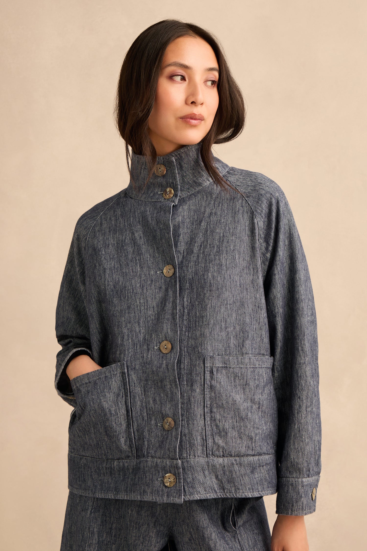 A woman wearing the Washed Cotton Linen Jacket in gray, featuring large pockets and paired with matching pants, stands against a plain beige background, gazing off to the side.