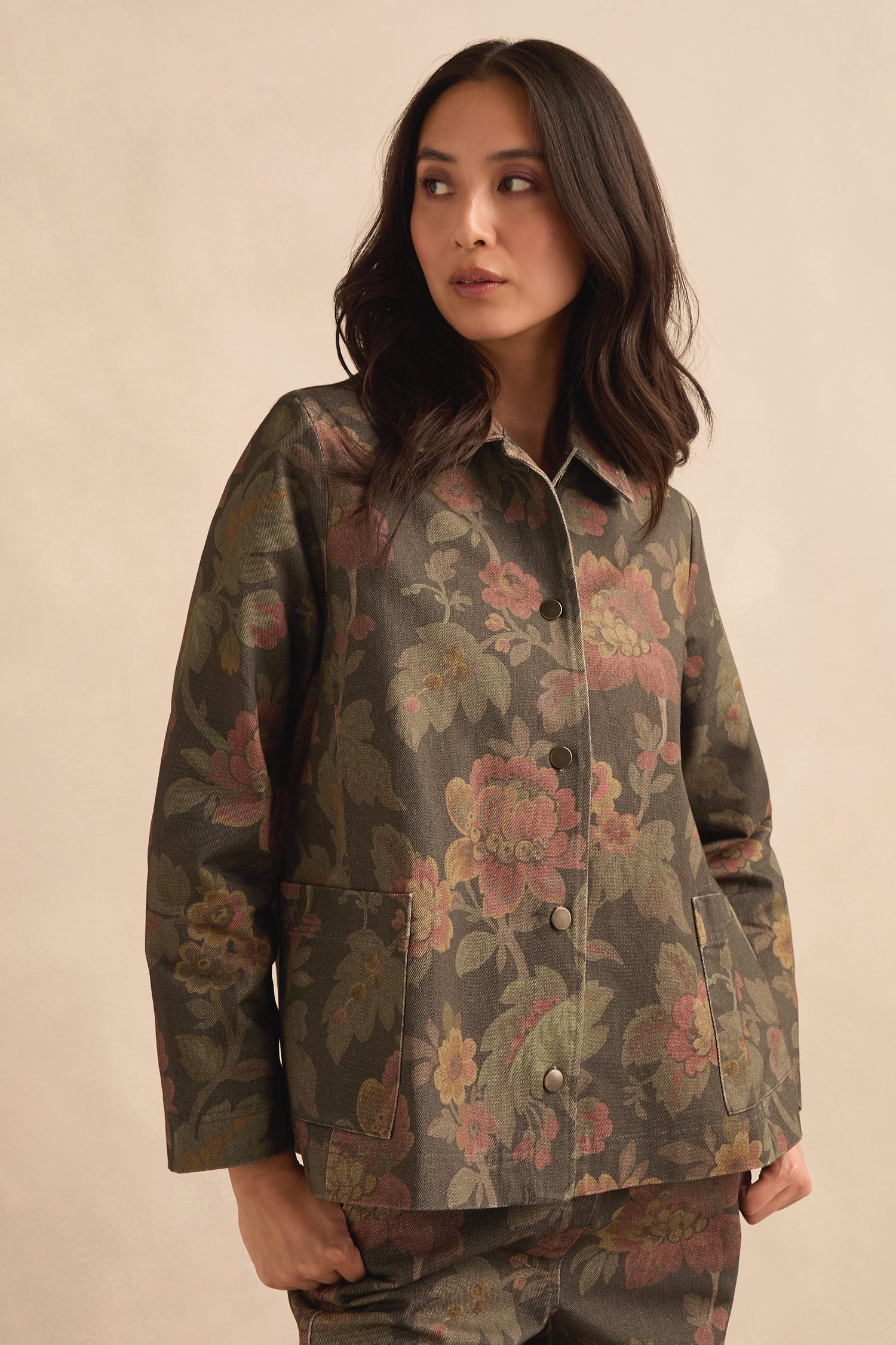 A woman wearing the Heirloom Damask Denim Jacket with a dark archive print and matching pants stands against a light beige background, looking to the side.