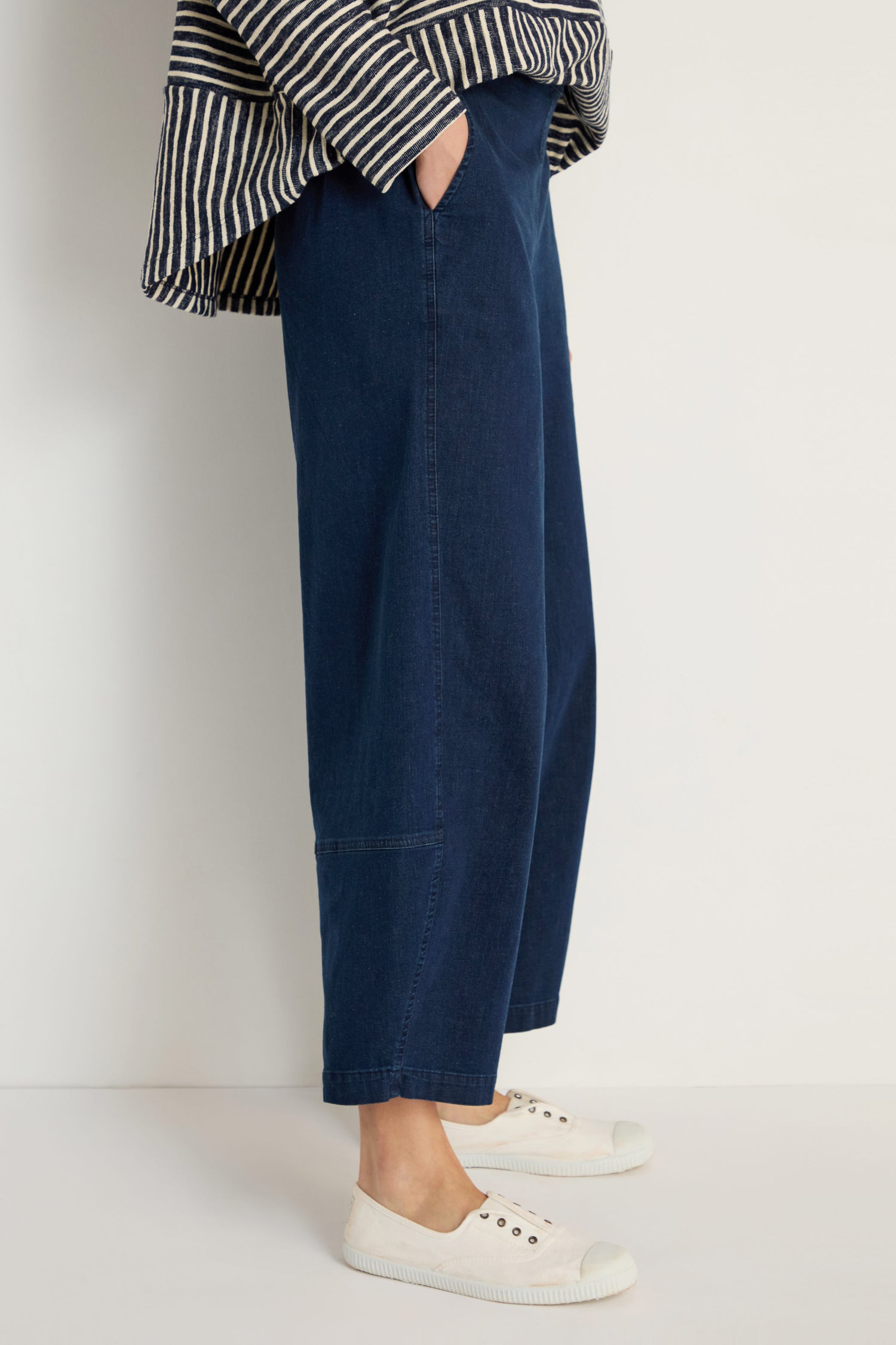Model wears the Stretch Denim Bubble Trouser in dark blue with a striped long-sleeve top and white sneakers, standing against a plain white background.