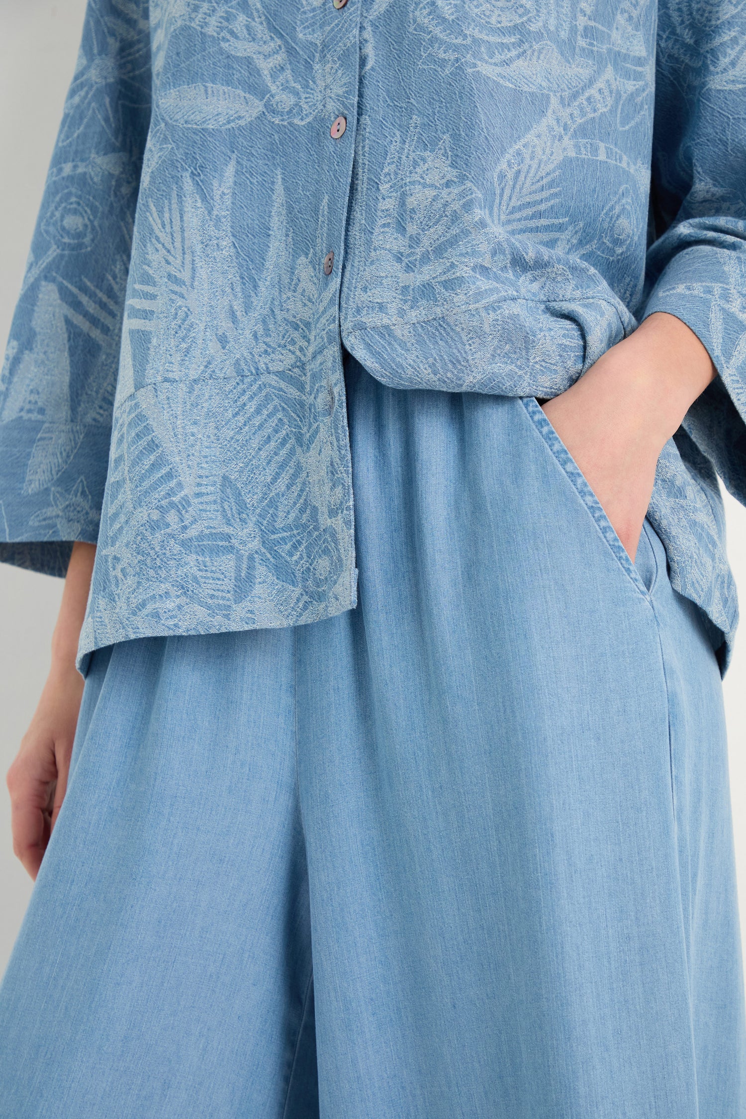 Person wearing Fluid Denim Wide Trousers and a light blue patterned button-up shirt, with one hand in their pocket.