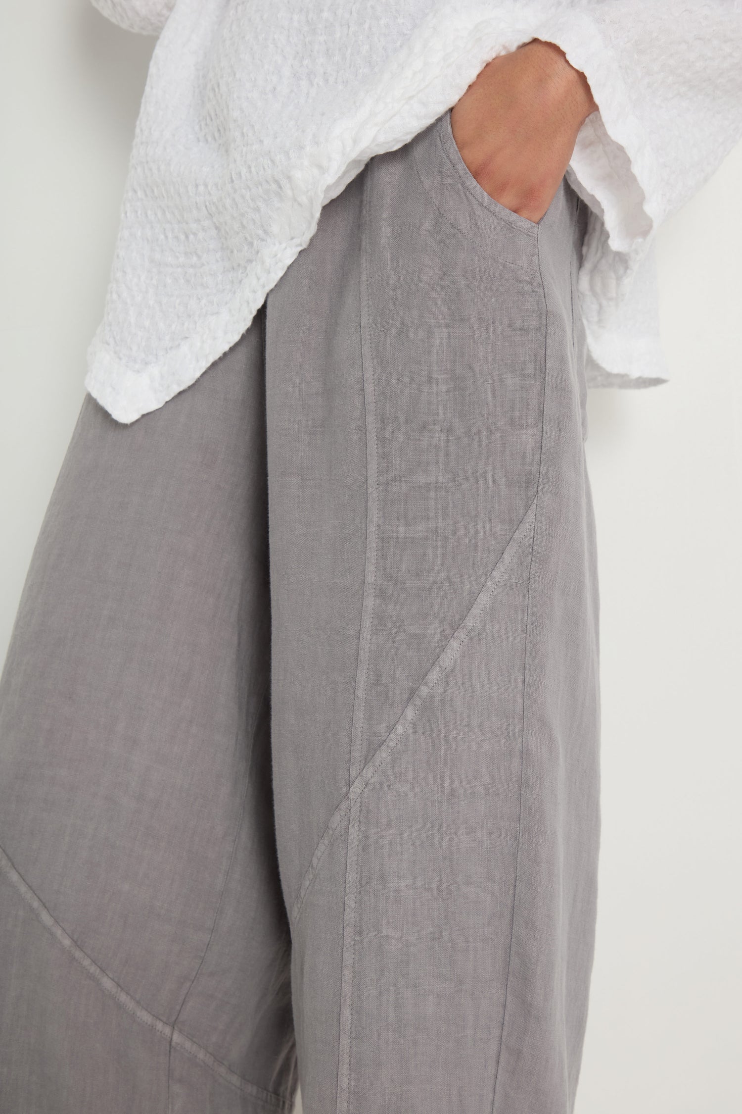 Wearing the Linen Curved Seam Bubble Trouser in light gray with a textured white top, one hand casually in the pocket.