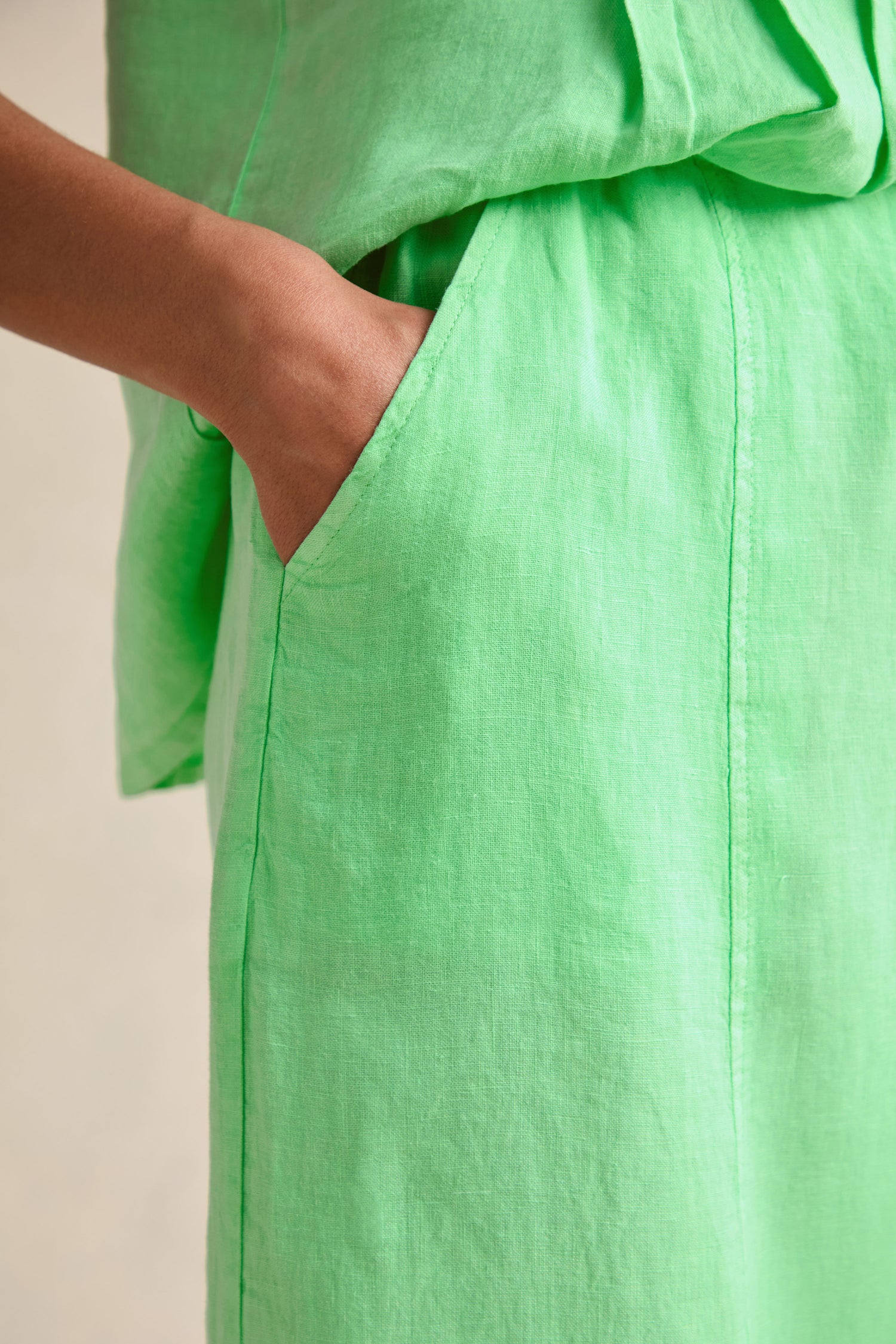A person’s hand rests in the pocket of the Linen Seam Detail Pistachio Bubble Trouser, made from light green linen and featuring subtle seam detailing.