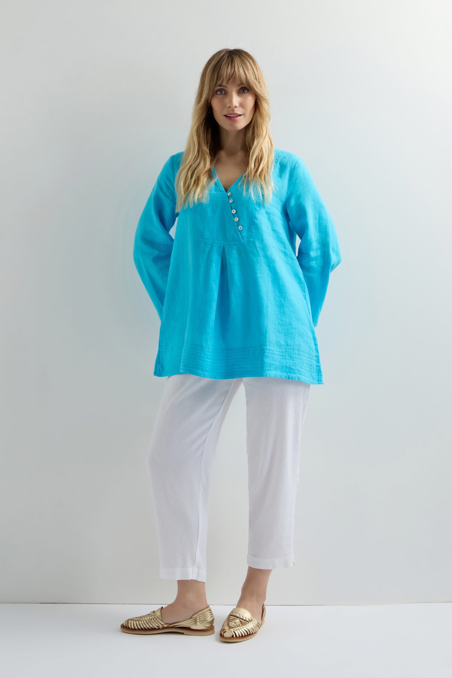 A person wears a vibrant blue Linen Button Placket Tunic with white pants, showcasing its classic fit against a plain white backdrop.
