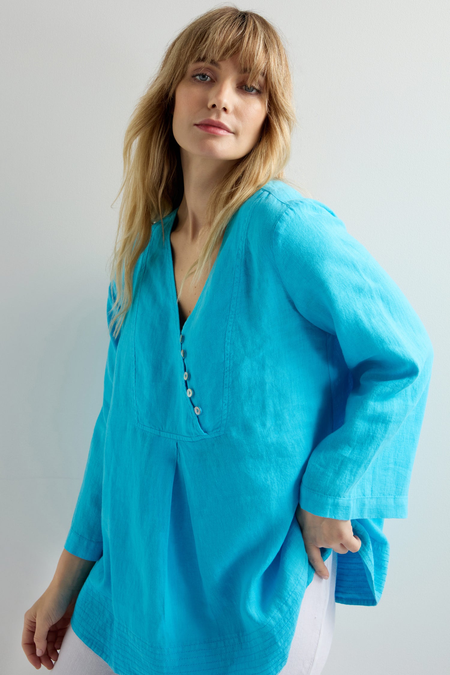 The Linen Button Placket Tunic, featuring a kaftan-inspired silhouette and a relaxed fit, stands against a light backdrop in vibrant bright blue.