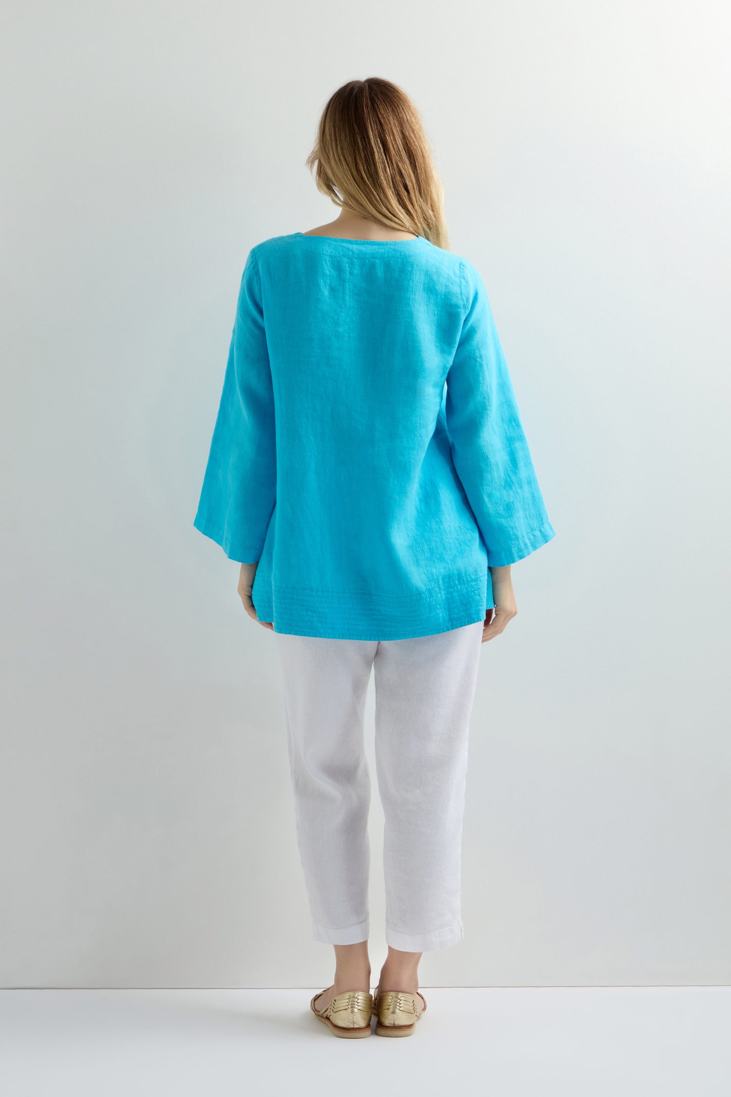 The relaxed fit Linen Button Placket Tunic, paired with white pants, showcases a kaftan-inspired silhouette as the wearer stands against a light background.