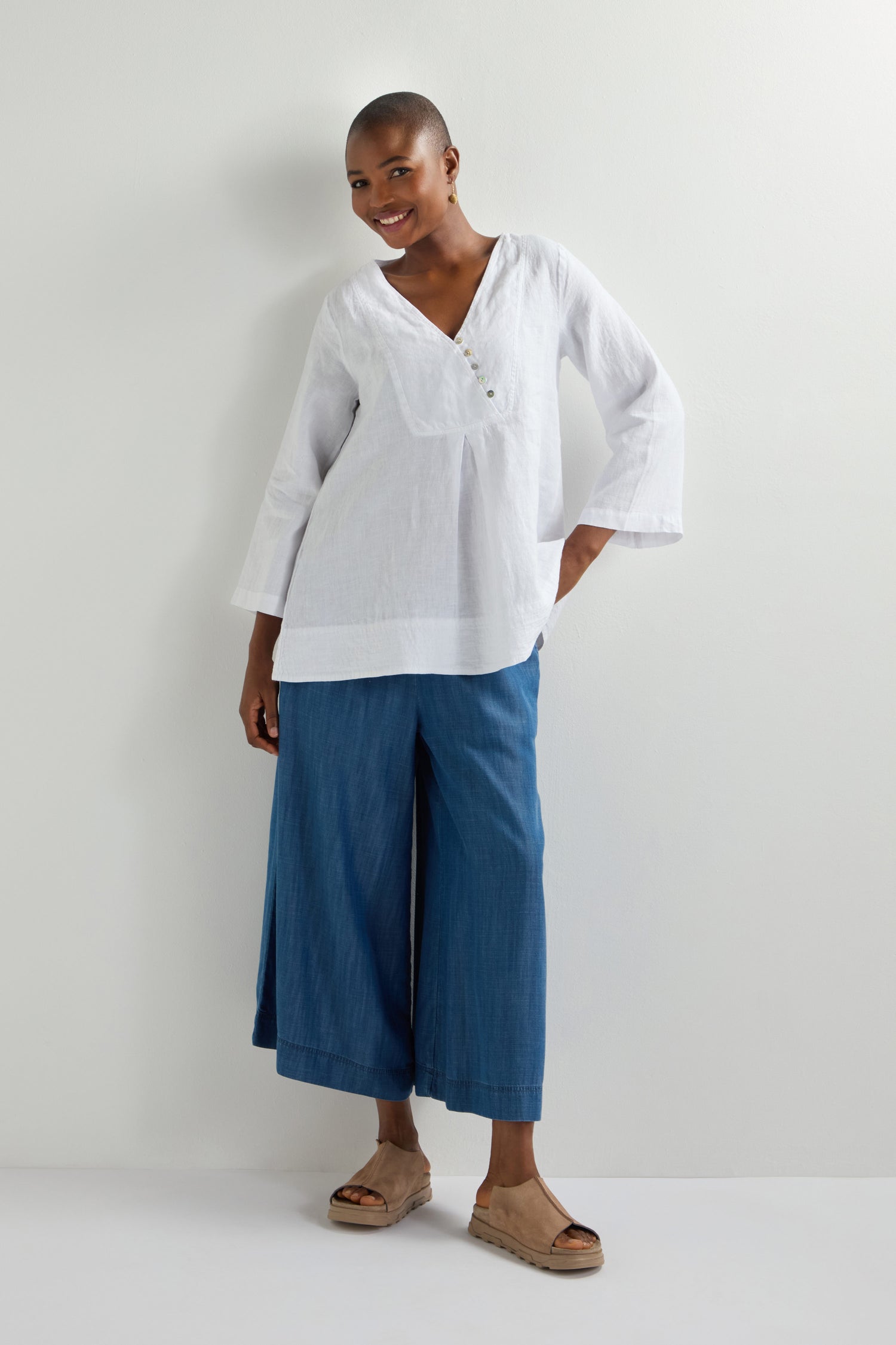 A person in a Linen Button Placket Tunic, blue wide-leg pants, and beige platform sandals stands against a plain white background.