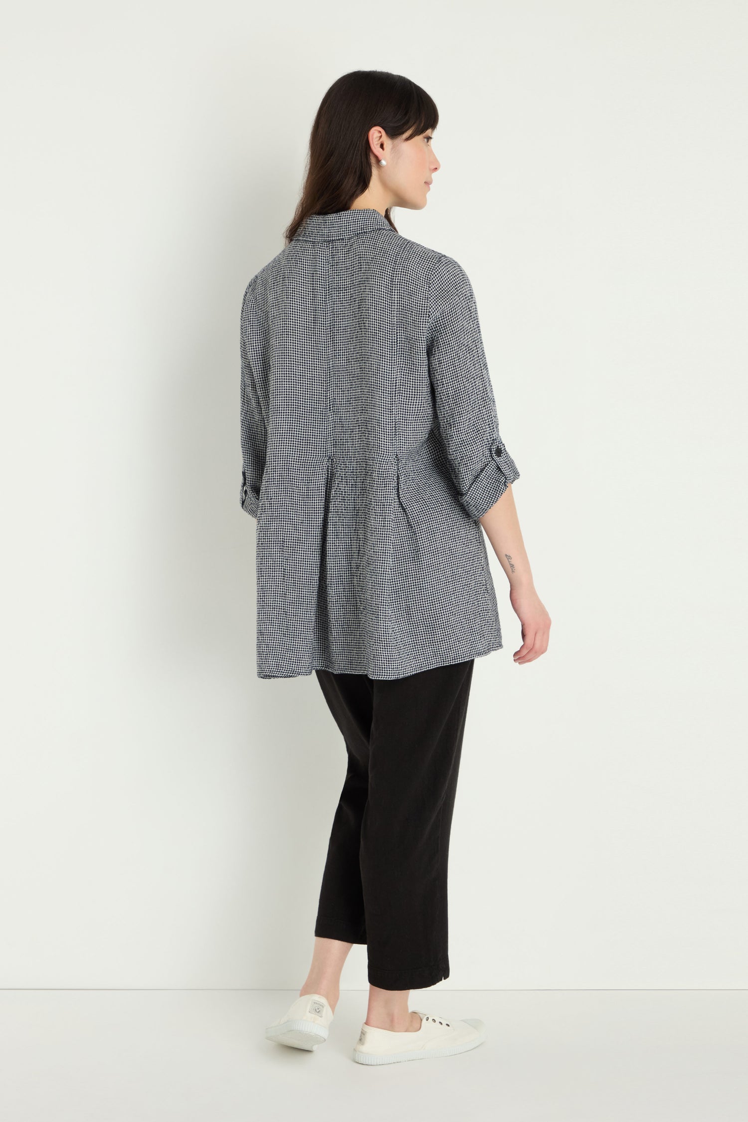 A woman, facing away against a white background, wears a grey textured jacket with rolled sleeves over the Micro Gingham Shirt, paired with black pants and white sneakers.