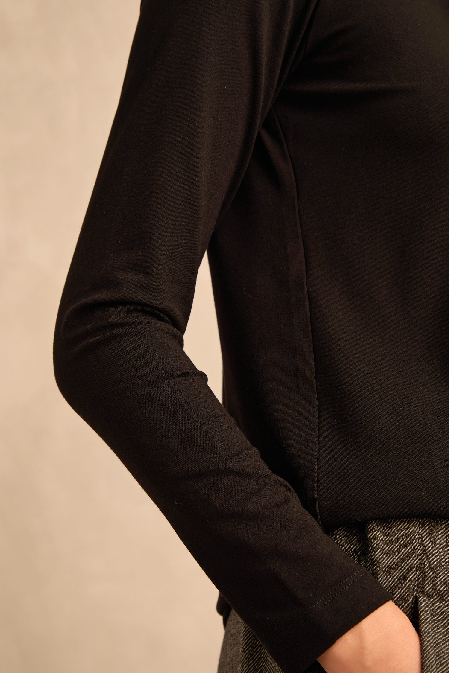 A person is shown from the shoulder to the waist against a neutral background wearing the Viscose Jersey Scoop Neck Top in black with gray pants.