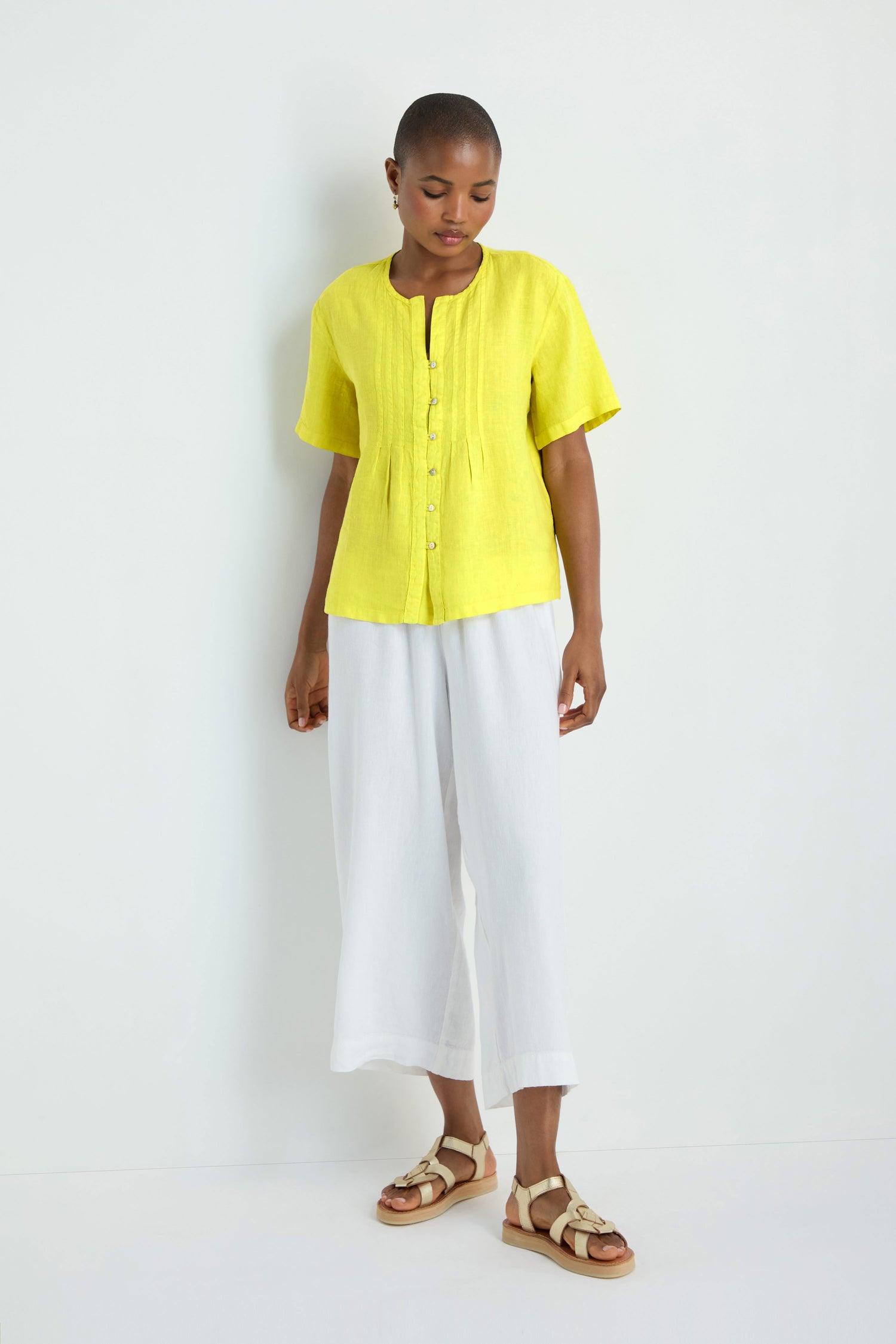 Model in a Linen Pleat Short Sleeve Lemon Shirt, white wide-leg pants, and beige sandals stands against a plain white background.
