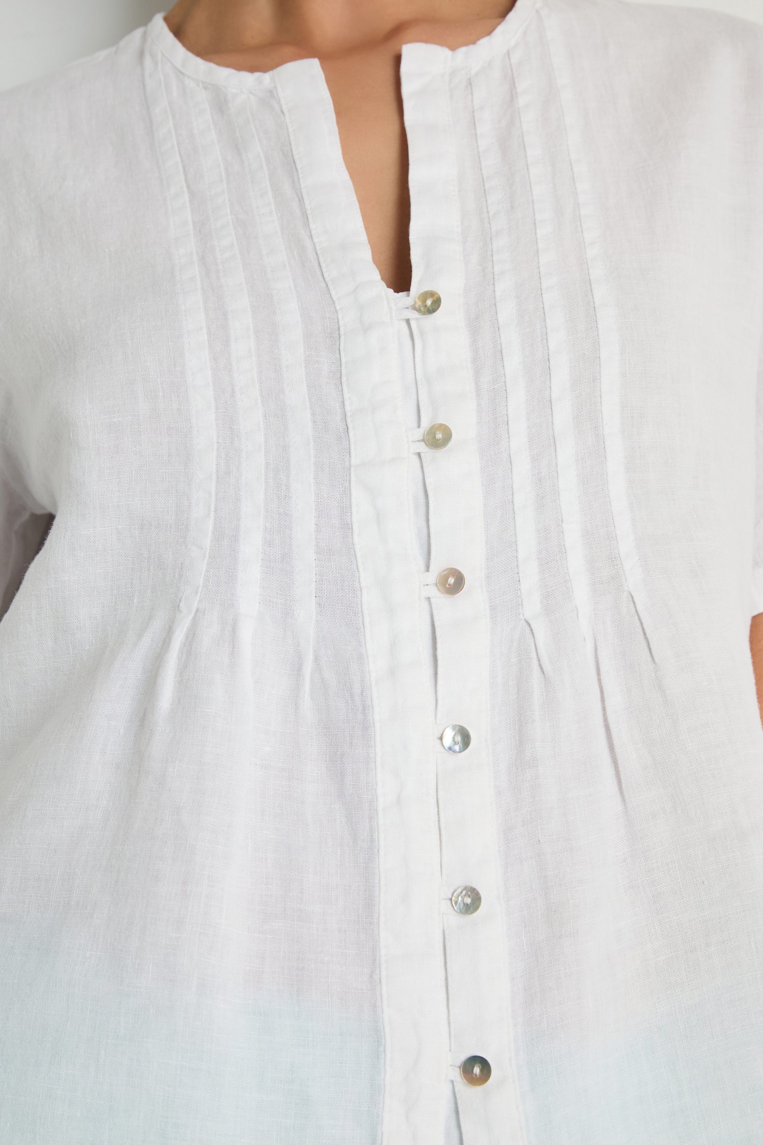 Close-up of the Linen Pleat Short Sleeve White Shirt, featuring vertical pleats and a button-down front, worn by a person.