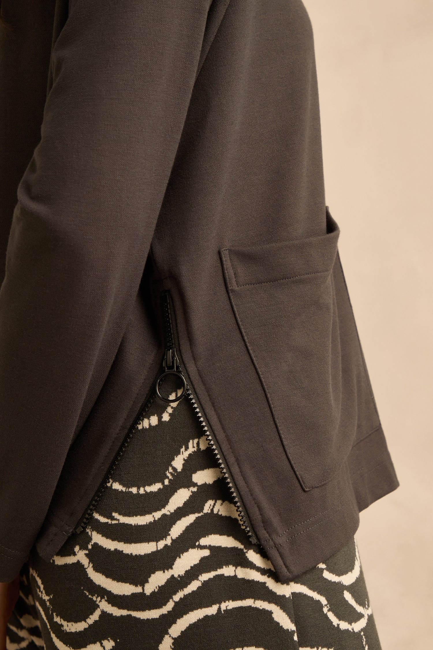 Close-up of a person wearing the Luxe Viscose Jersey Cowl Neck Top with a side zipper and pocket, paired with a patterned black-and-white skirt.