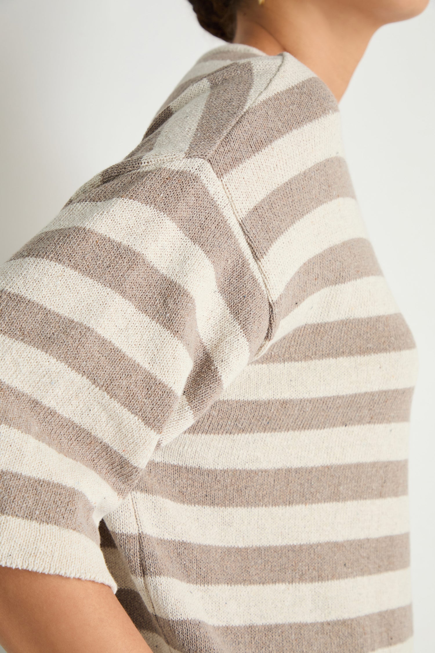 Model wearing the Striped Cotton Tunic, featuring beige and white stripes with short sleeves, shown from the side against a plain background—a perfect layering piece for casual outfits.
