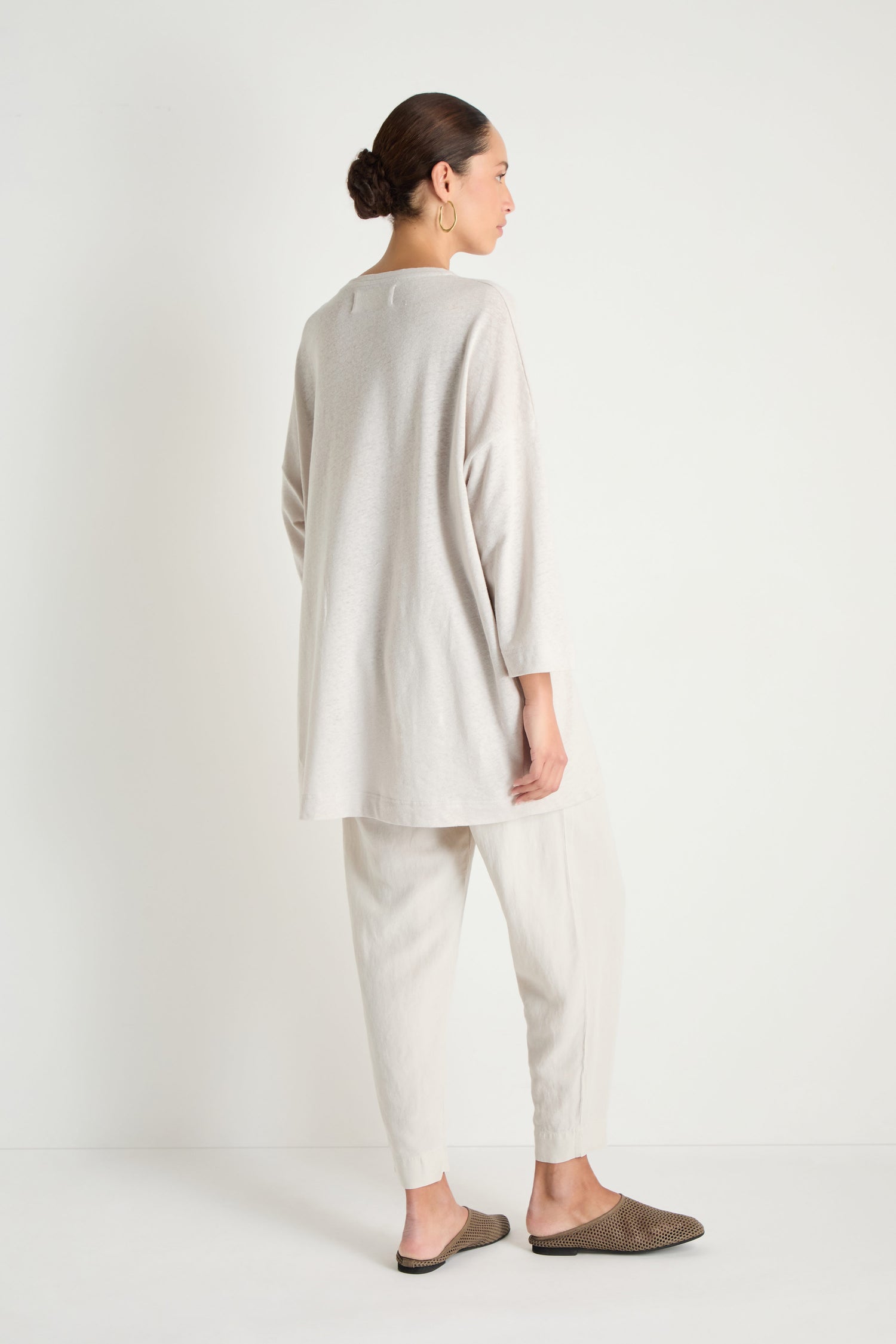 A woman, seen from behind, models the Linen Cotton Jersey Tunic with matching pants and slip-on shoes, highlighting its relaxed fit against a plain white backdrop.