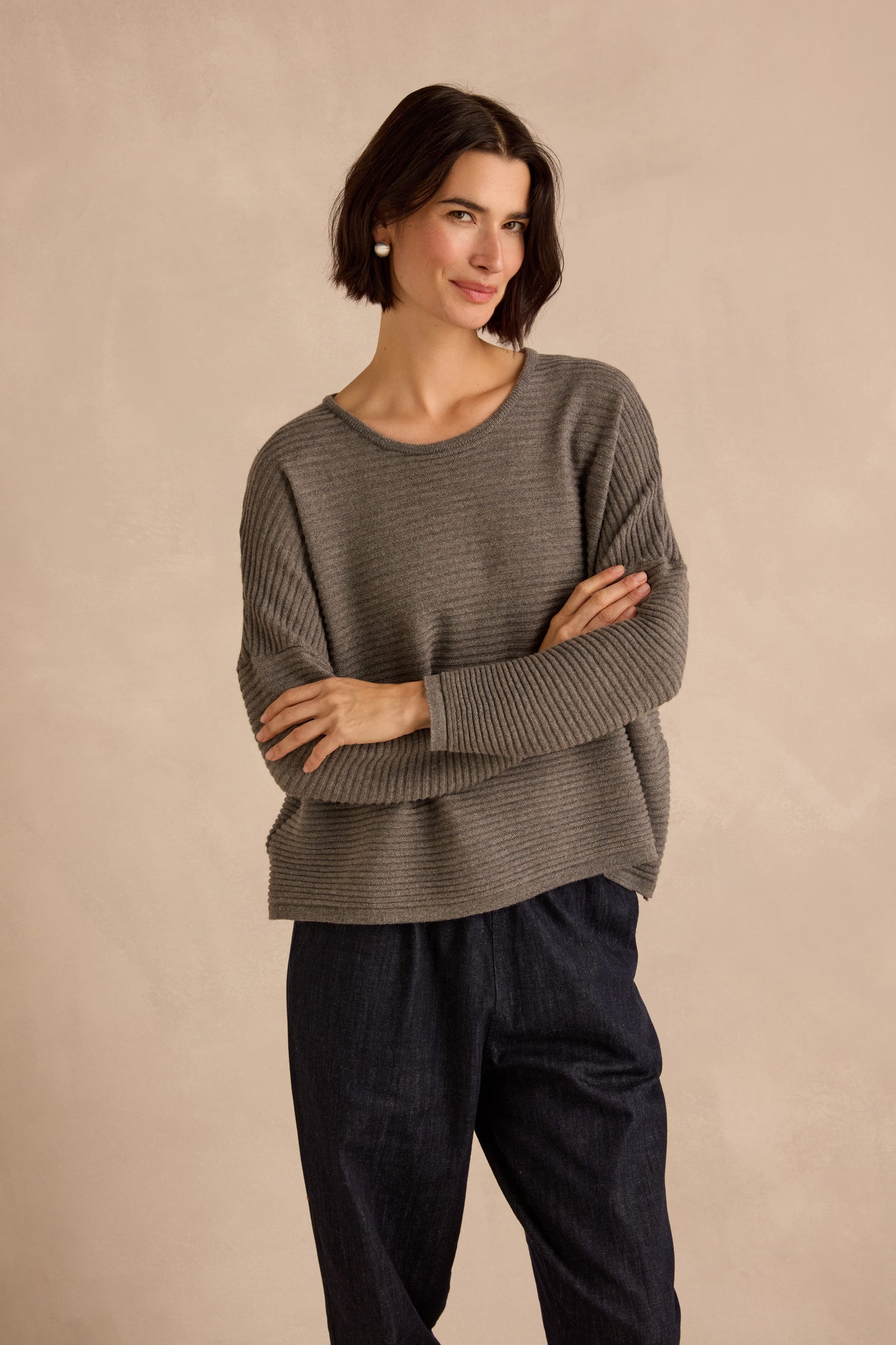 Woman wearing the Mole Fine Rib Merino Top in gray and dark pants stands with arms crossed against a beige background.