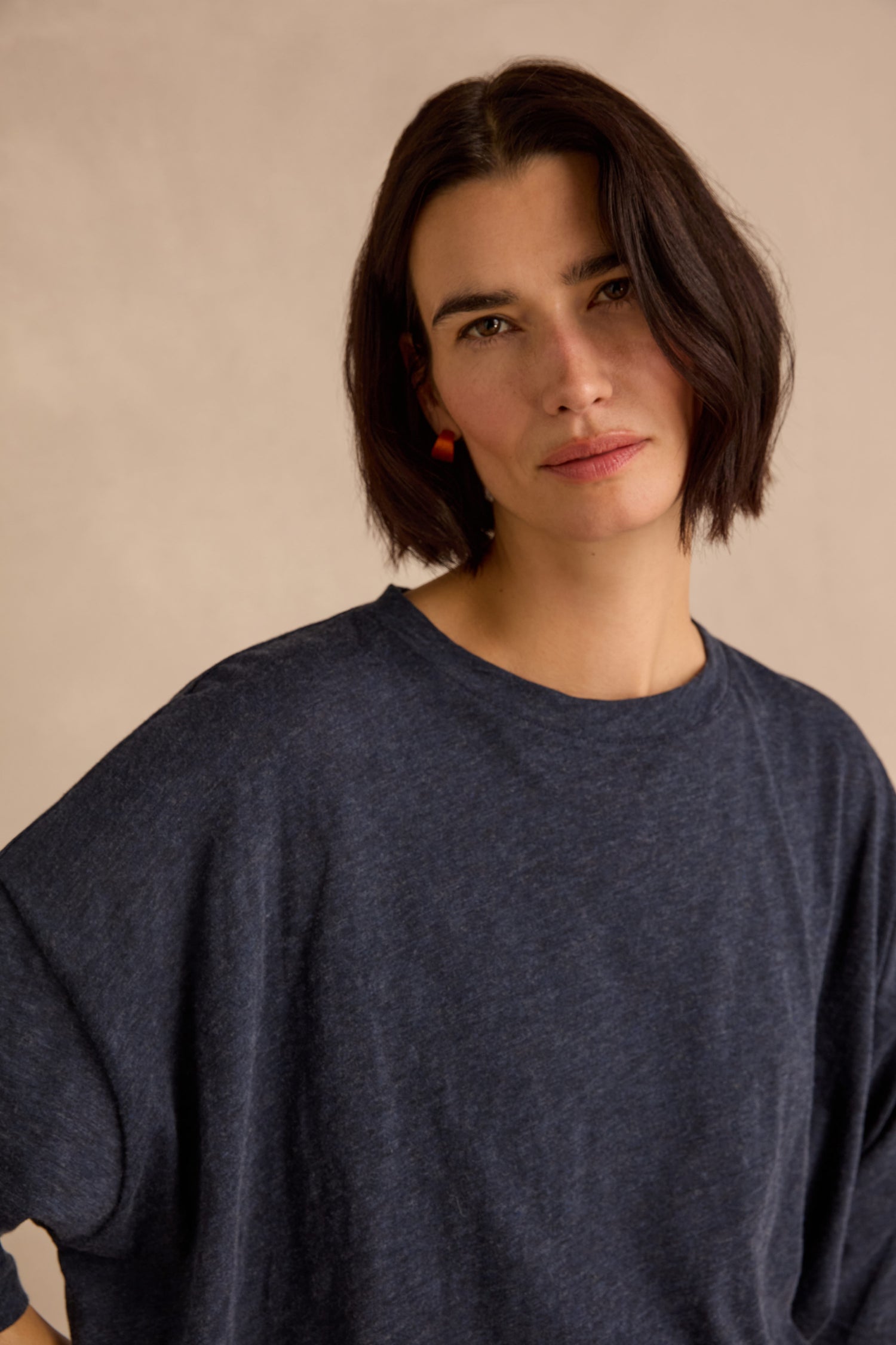 A woman with shoulder-length dark hair wears the Cotton Wool Jersey Tunic in navy, showcasing its relaxed silhouette and soft fabric, as she stands against a neutral background looking at the camera with a neutral expression.