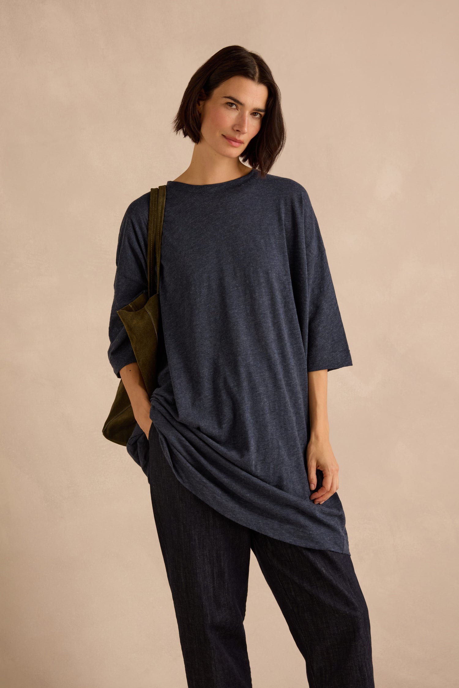 A person with short dark hair wears the Cotton Wool Jersey Tunic in a loose-fitting navy style paired with dark pants, carrying an olive green shoulder bag and standing against a neutral background for a relaxed silhouette.