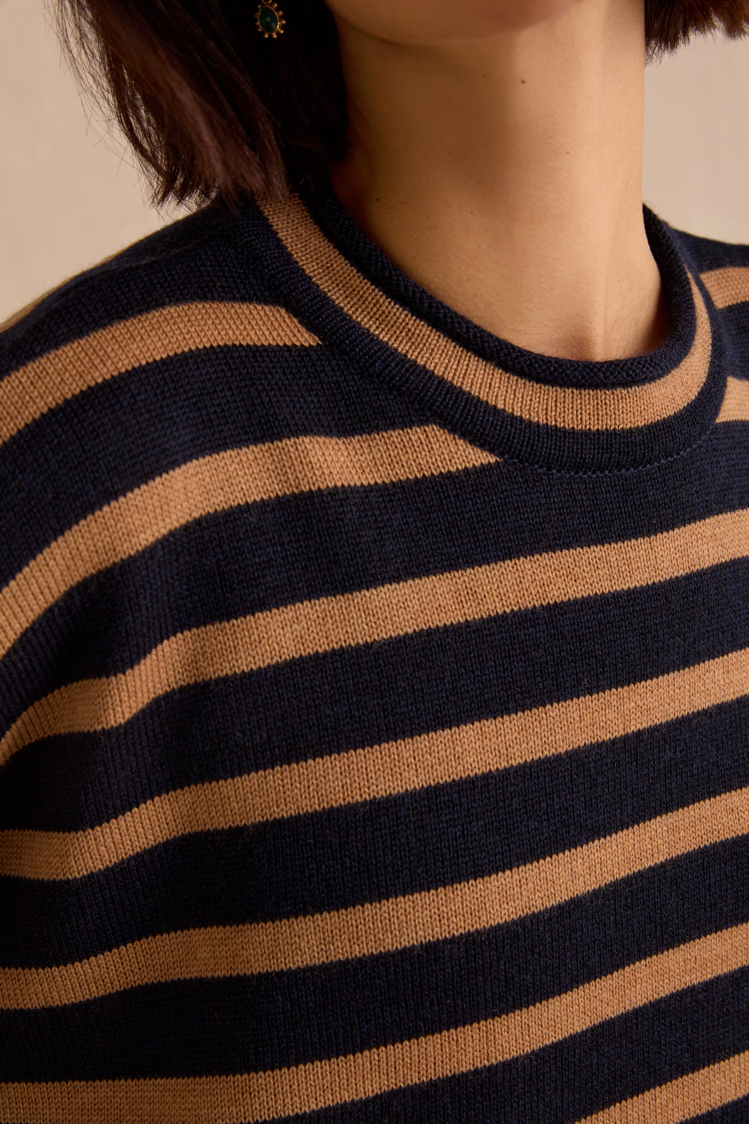 A person wearing the Navy Stripe Boxy Merino Knit sweater, featuring a boxy fit with navy blue and tan horizontal stripes, shown from the shoulders to upper chest with part of their face not visible.