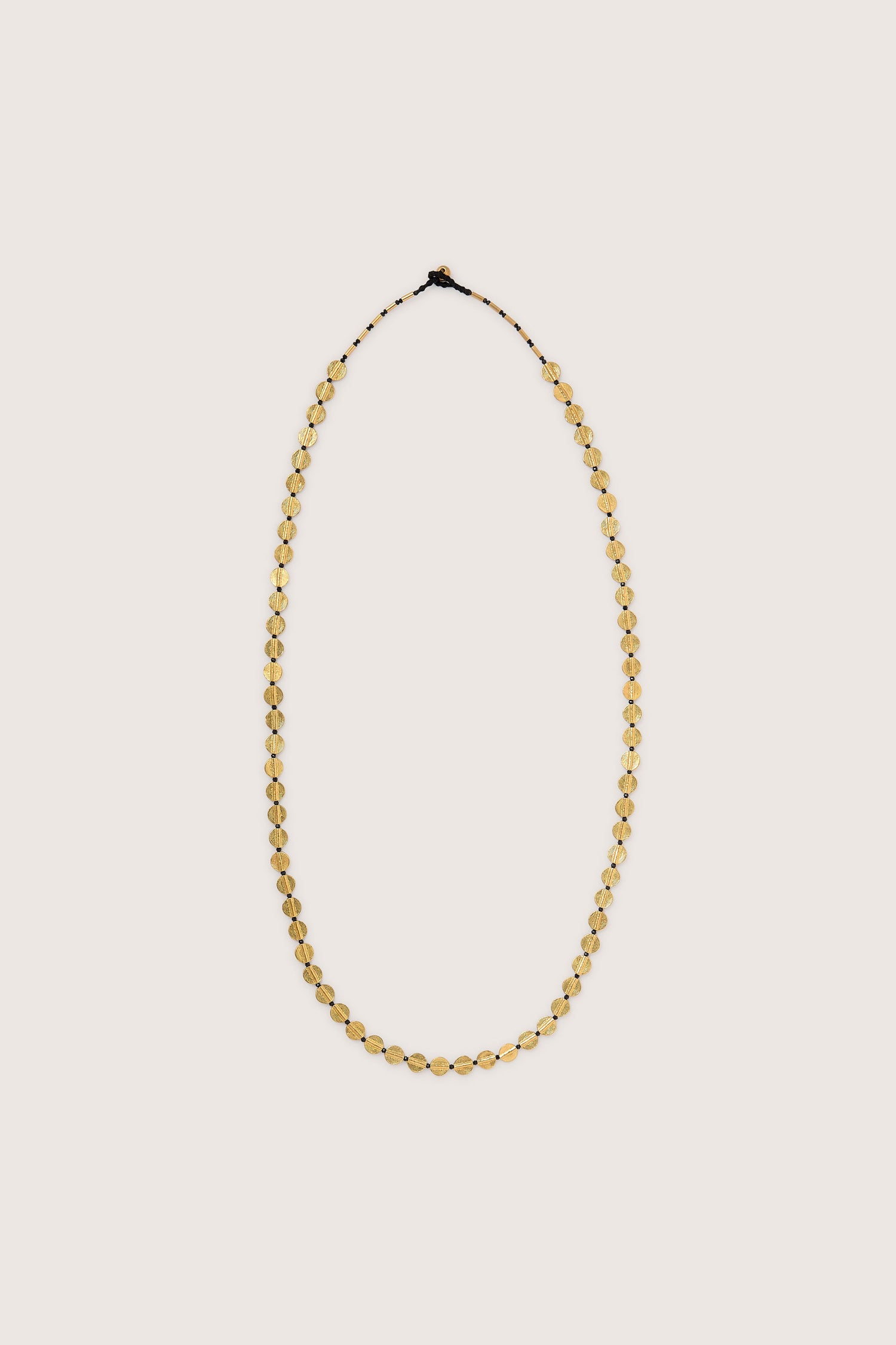 The Long Engraved Circles Necklace features small, oval-shaped yellow beads set along a thin, dark string in Jaipur artisan style, beautifully displayed on a plain light background.