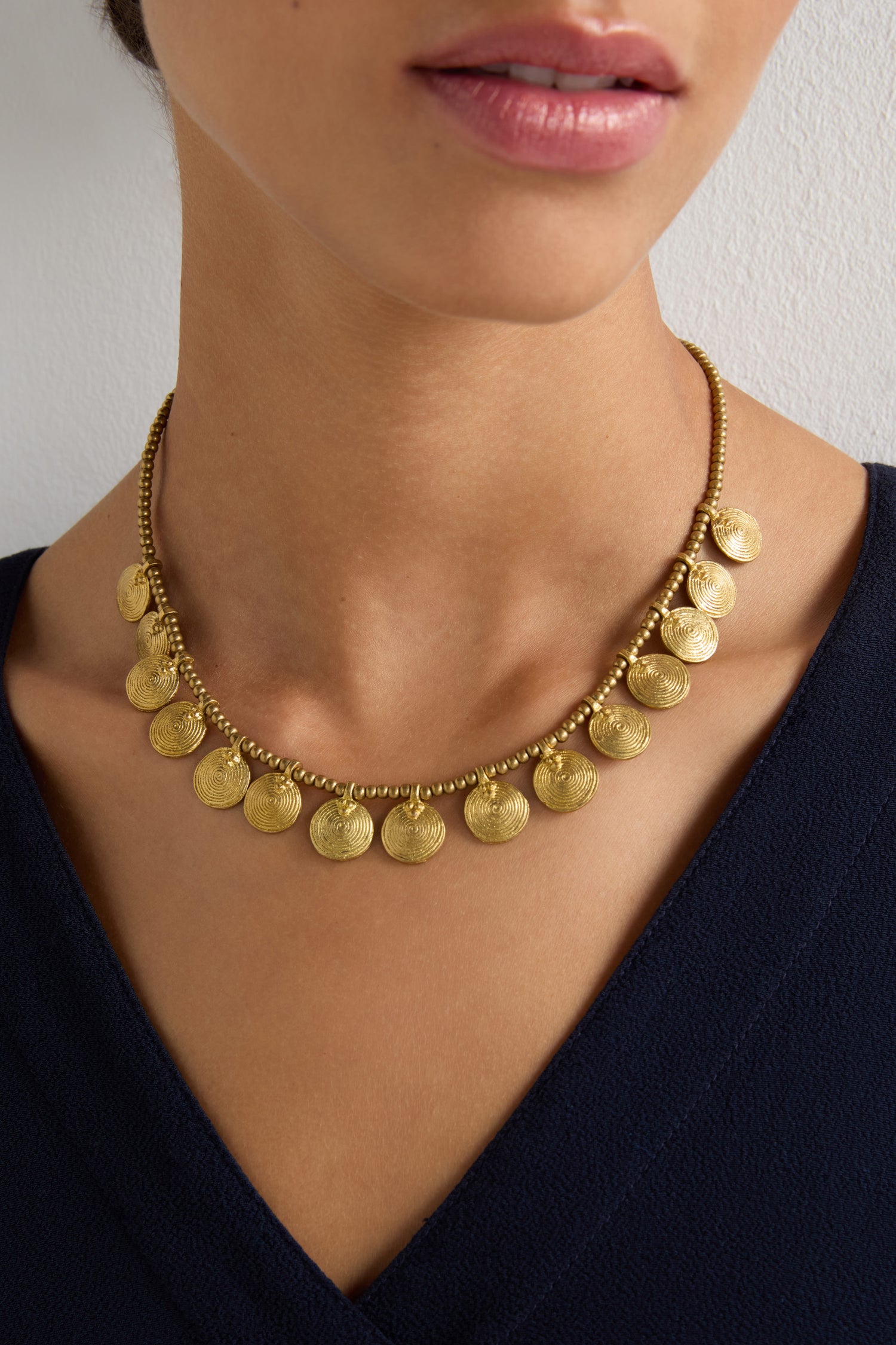 A person wearing a Short Gold Chakra Necklace with golden discs and a dark V-neck top, creating a timeless statement.
