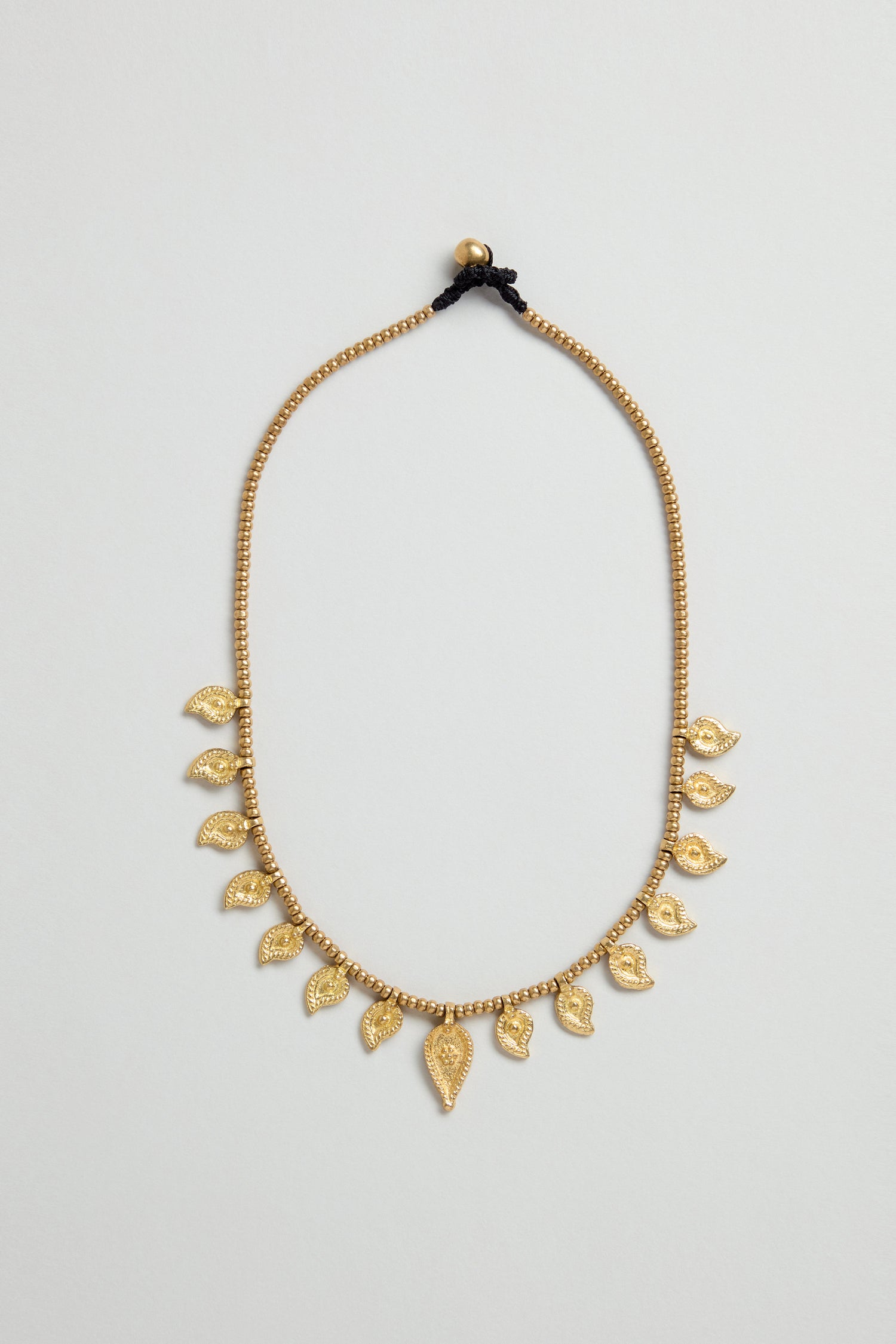 Paisley Necklace featuring gold beading, eleven leaf-shaped charms, traditional Indian metalwork, and a black thread tie closure, showcased on a plain light background.