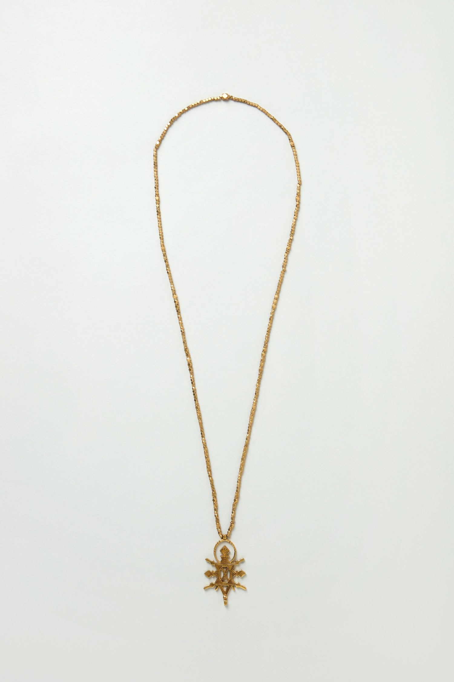 The Abalak Pendant features a striking spider-shaped gold tone chain necklace with small beads, shown on a plain white background.