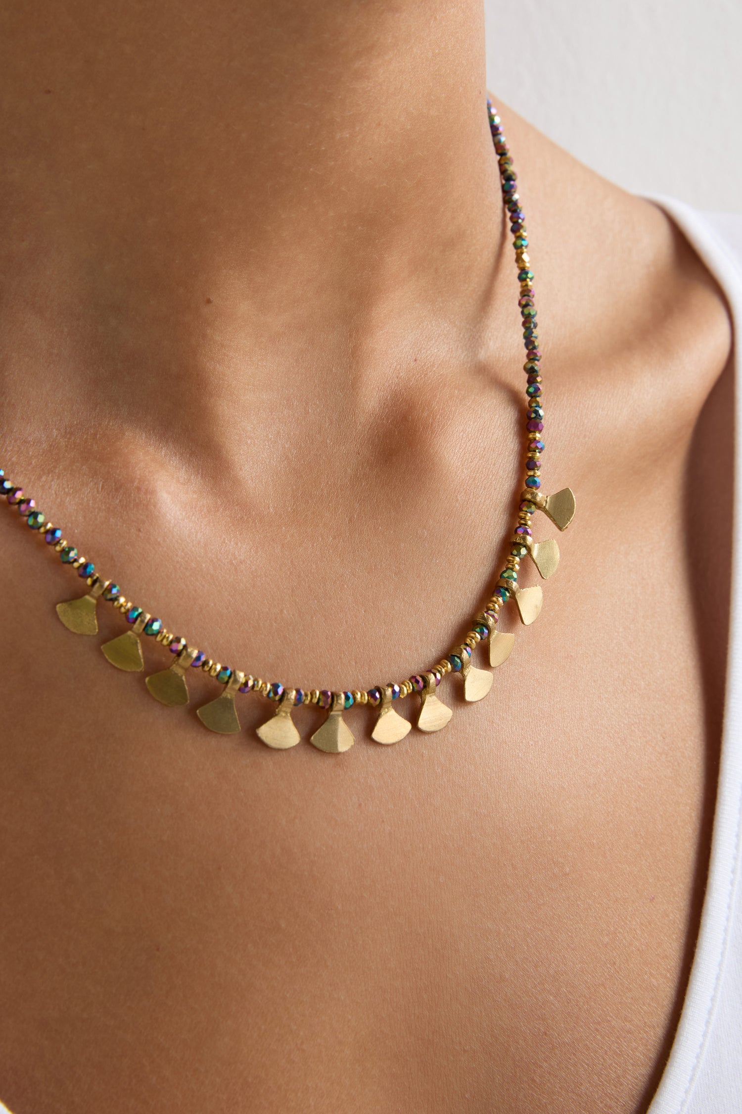 A close-up of a person wearing the Short Golden Petal Necklace, featuring gold petals and multicoloured beads, paired with a white top.