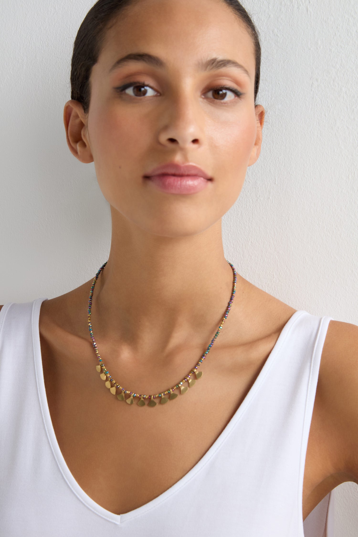 A woman in a white sleeveless top wears a Short Golden Petal Necklace, standing against a plain light background.