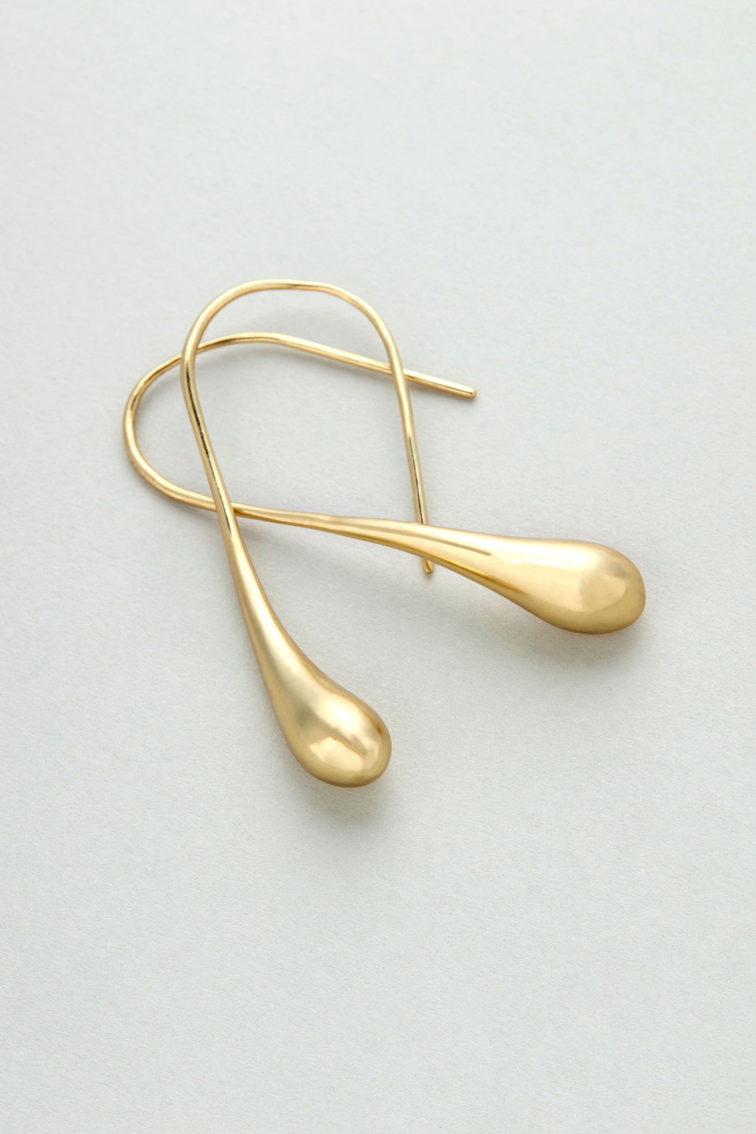 The Gilded Teardrop Earrings are handmade gold drop earrings with teardrop-shaped ends, showcased on a light, neutral background.