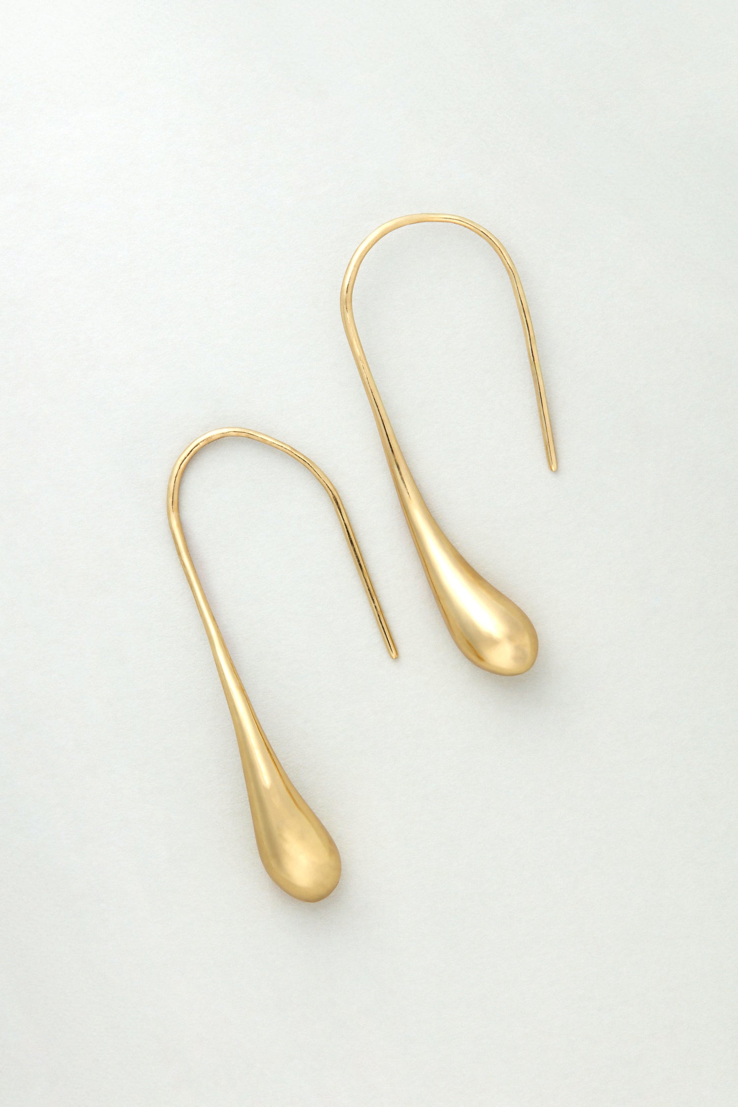 The Gilded Teardrop Earrings are handmade gold drop earrings with curved hooks, shown on a light gray background.