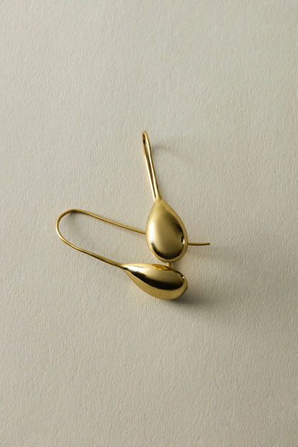 Ideal for a chic summer look, the Gold Gilded Teardrop Earrings rest gracefully on a light textured surface.