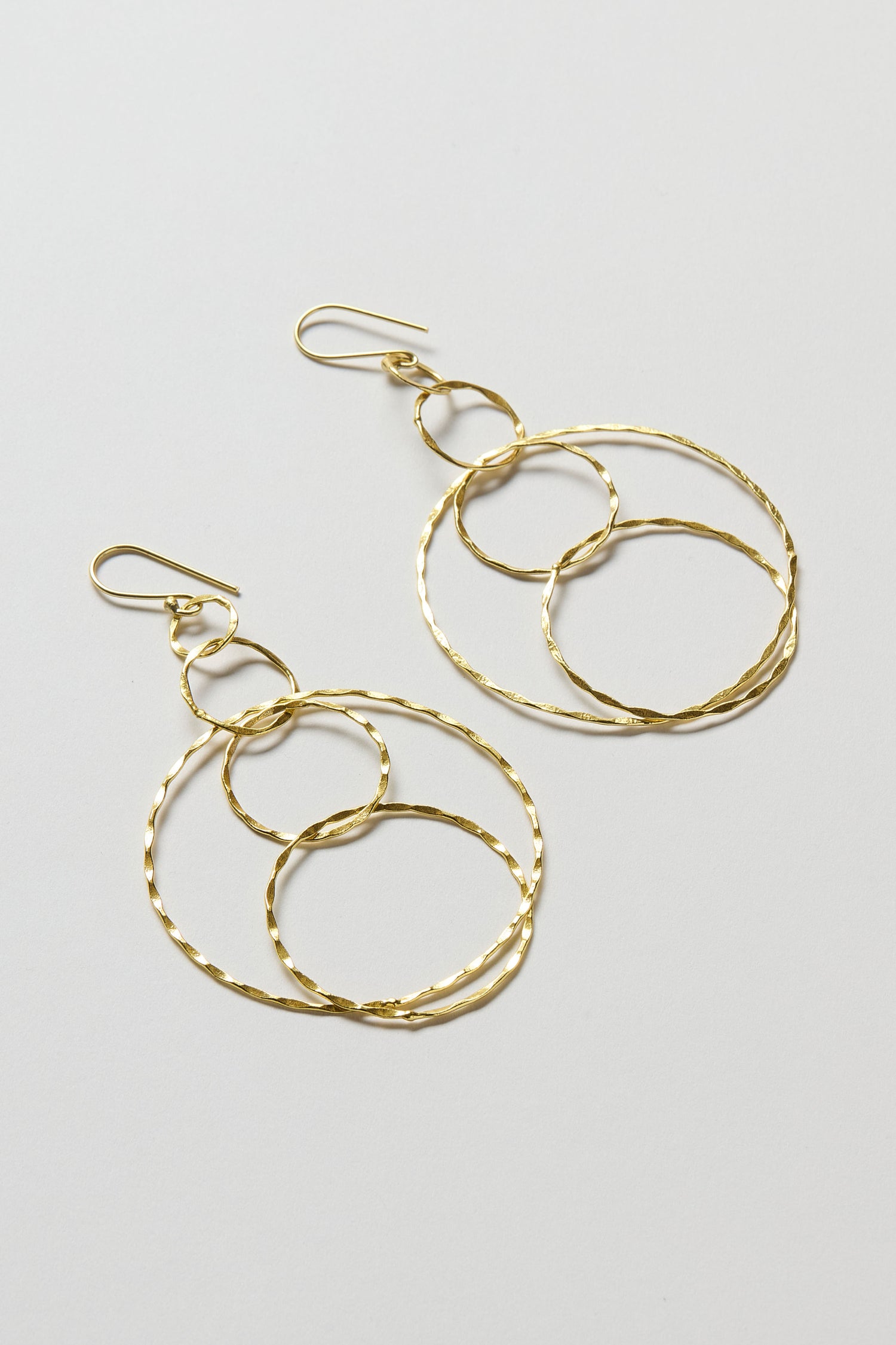 Dharma Earrings from the Nataraj Collection, featuring three interlocking textured gold-finished hoops, displayed on a light gray background.