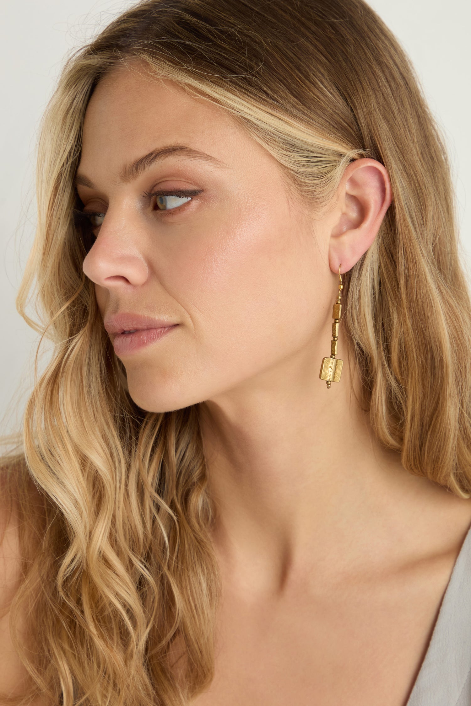 Woman with long blonde hair looks to the side, wearing a light top and the Engraved Squares Earrings—sculptural brass dangle earrings in a geometric style.